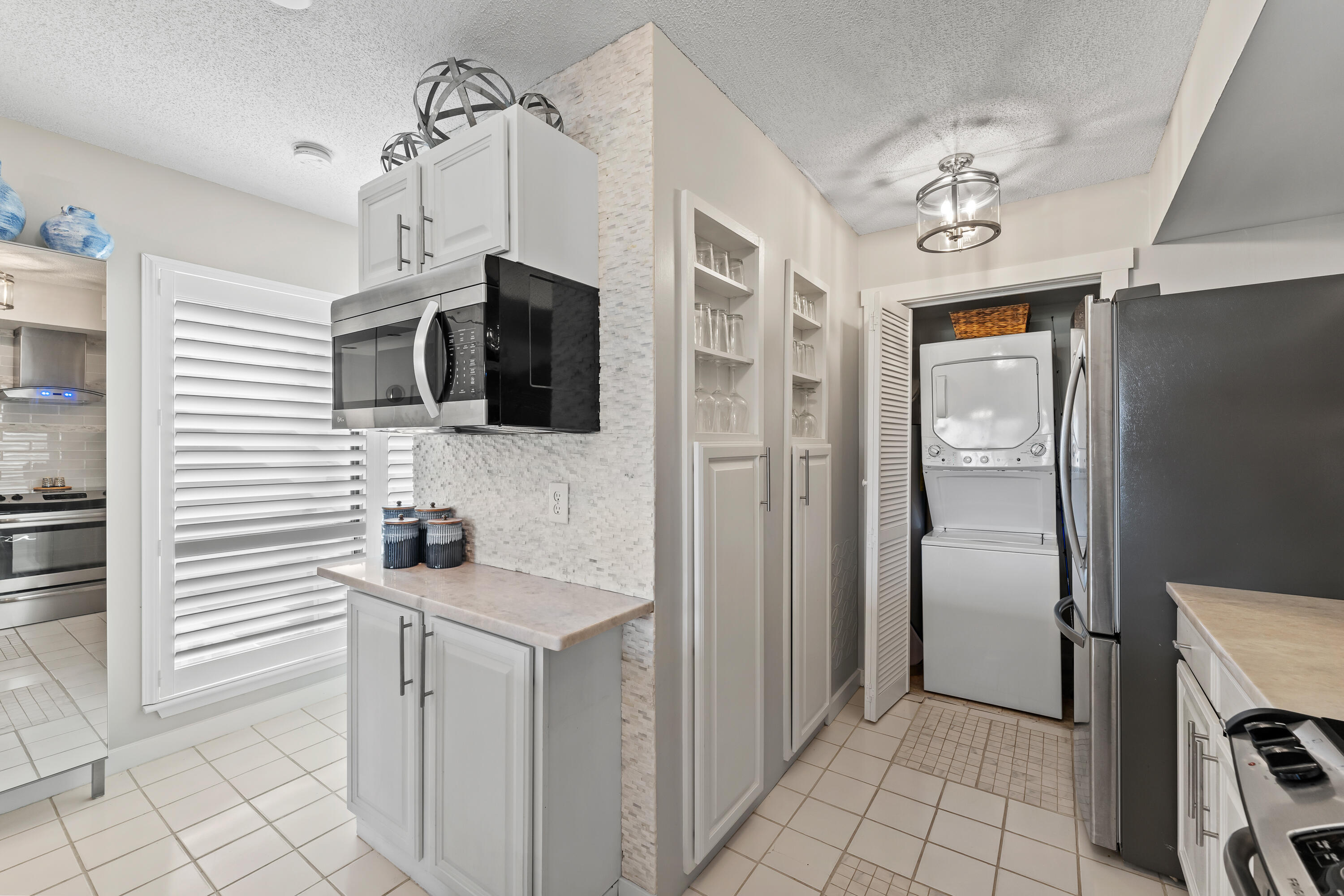 White kitchen with stainless appliances and a stacked washer and dryer in a laundry closet.