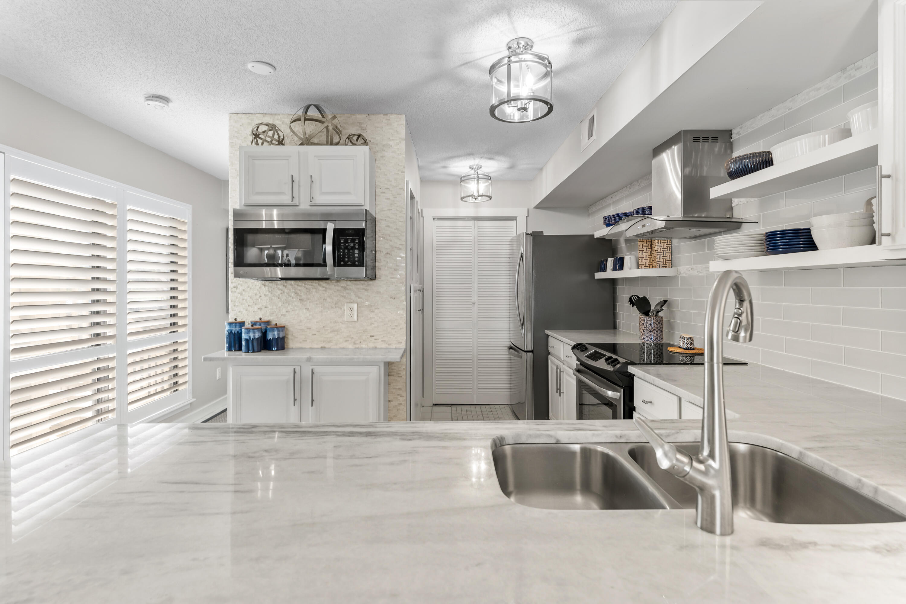 Bright kitchen with stainless steel appliances, open dish shelves, and a marble-look island with sink.