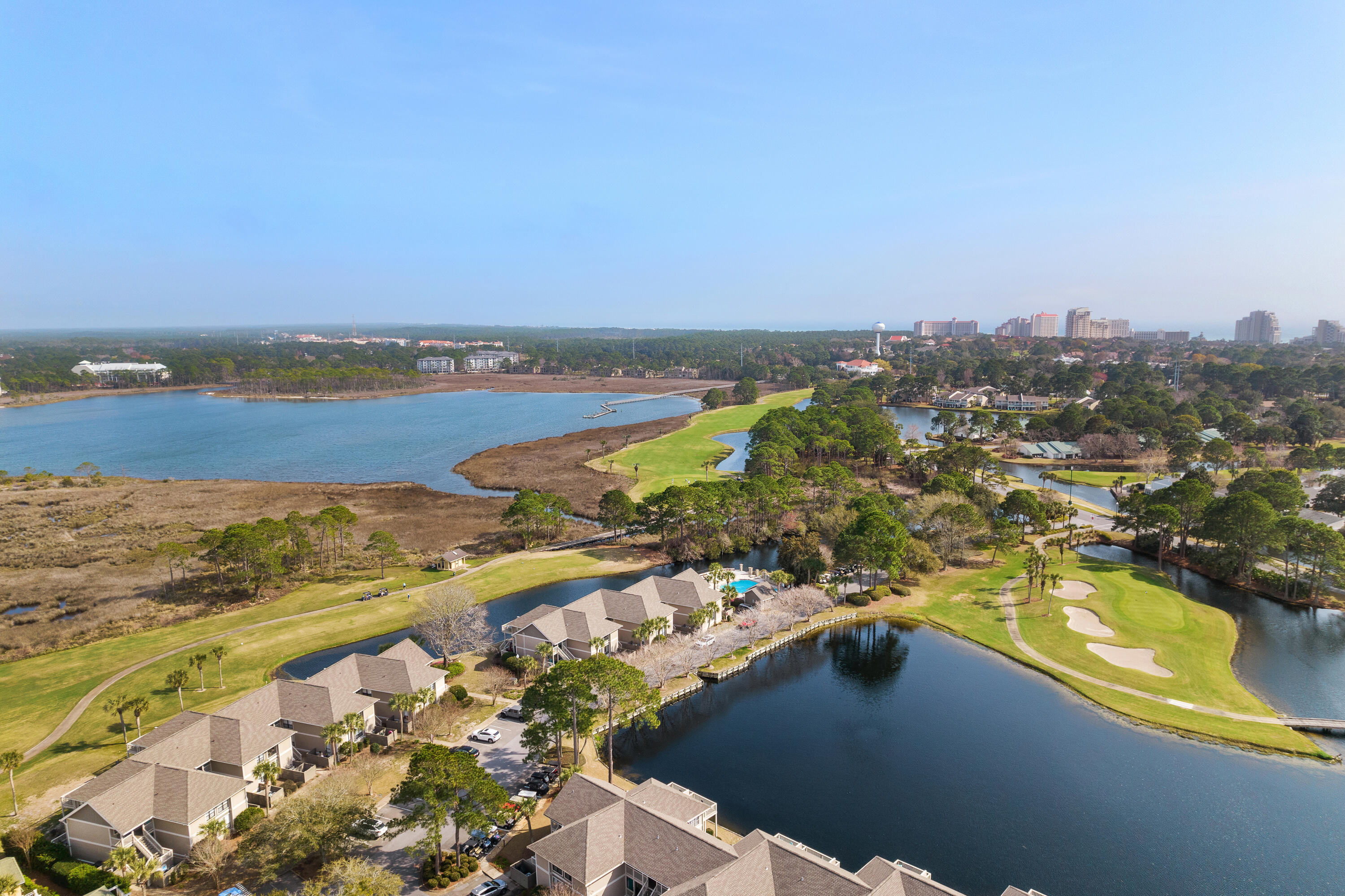 Aerial view of waterfront homes beside a golf course, lagoon, and marshland.