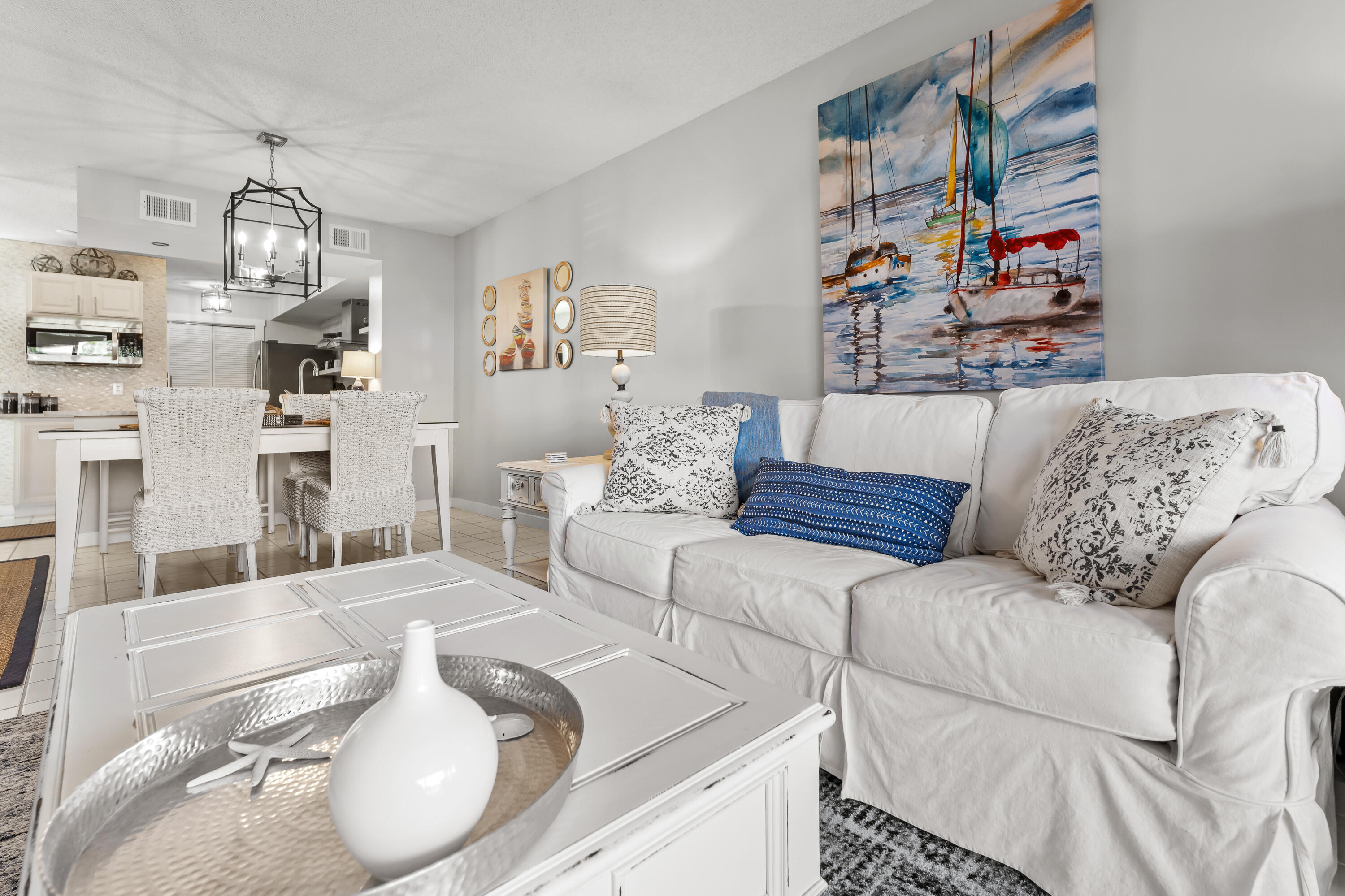 Furnished living room with a white sofa, sailboat painting, and open dining area and kitchen.