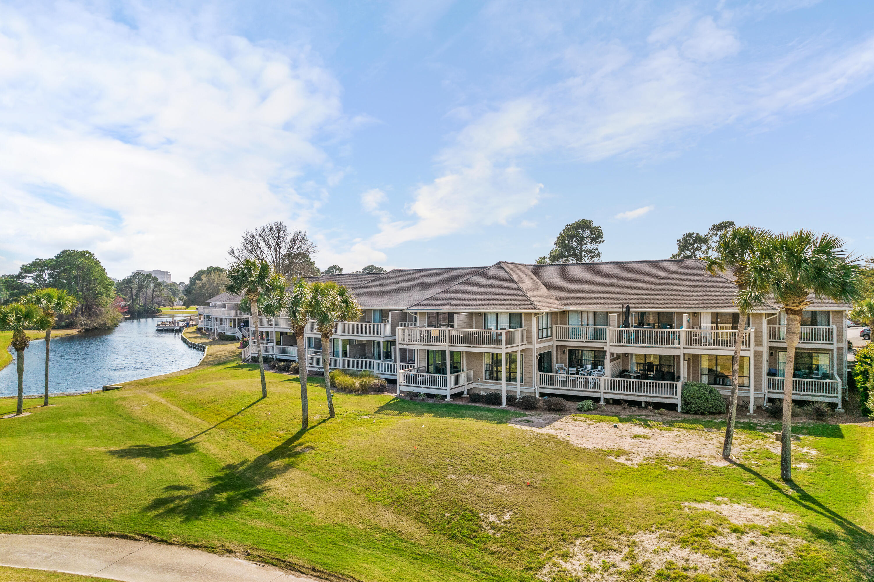 Waterfront condominium with rows of balconies beside a pond and palm-lined lawn.