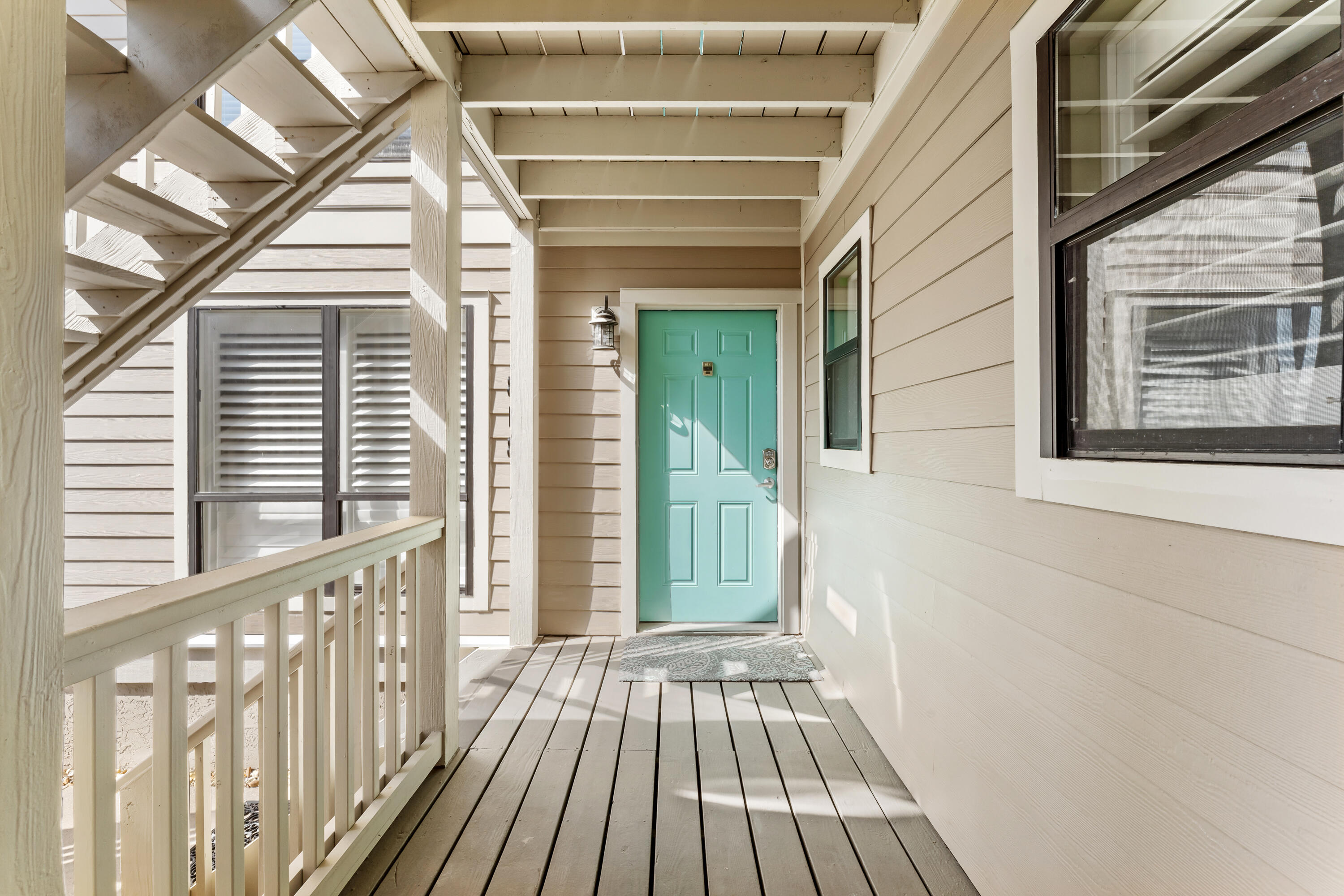 Covered porch with a turquoise front door, wood-plank deck, and staircase overhead.
