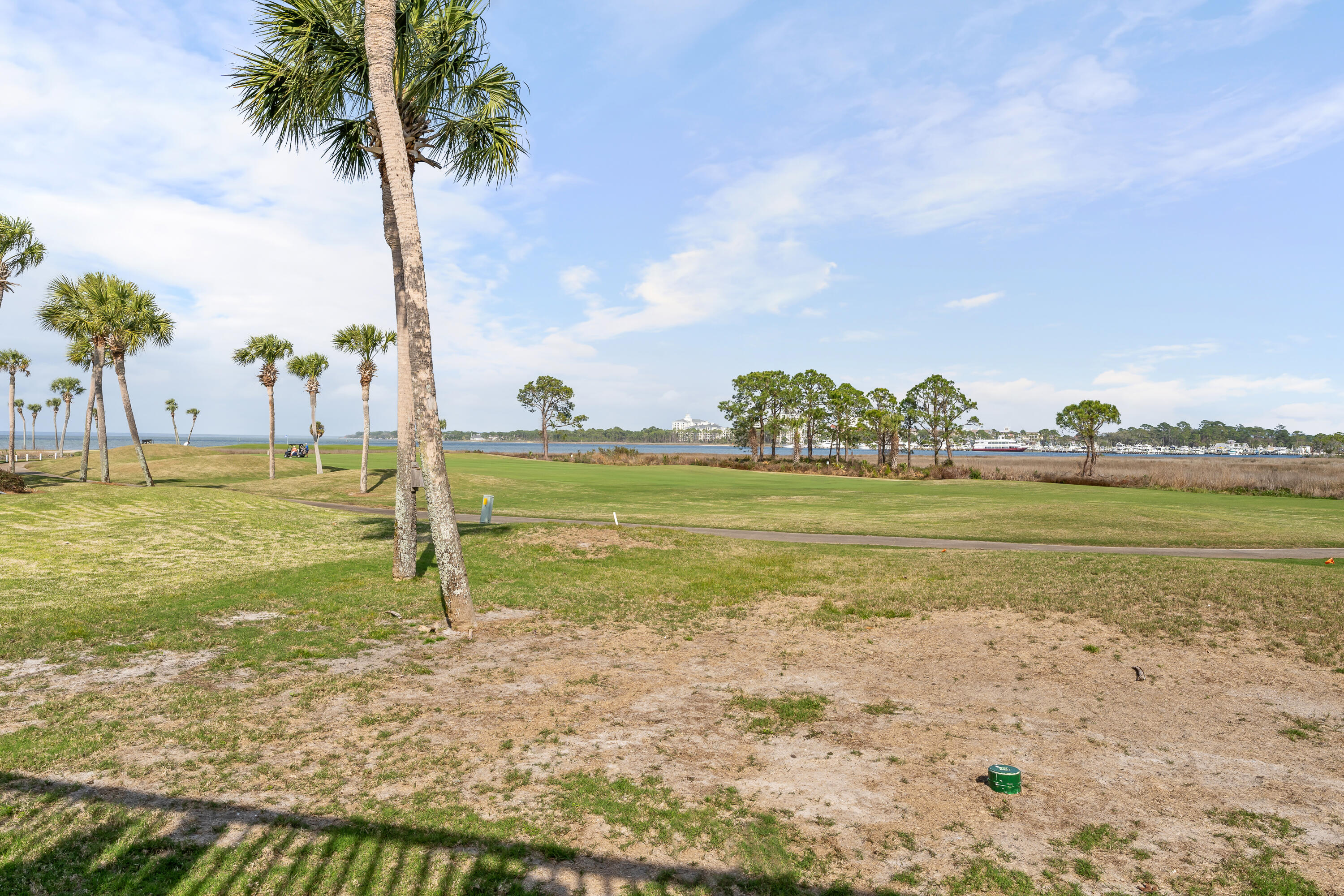 Waterfront golf course with palm trees and a bay in the distance.