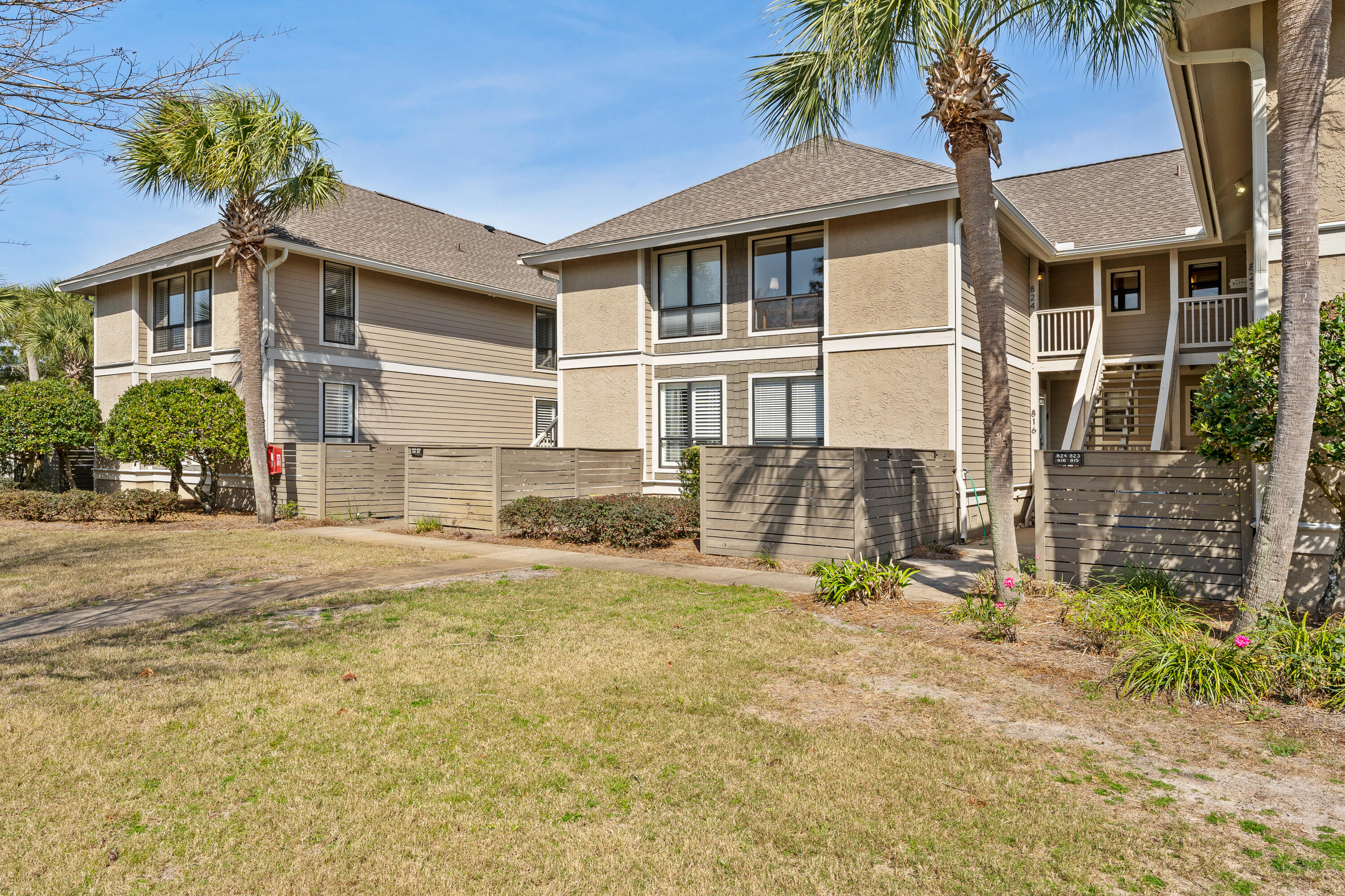 Two-story beige condominium with fenced patios, exterior stairs, and palm trees.