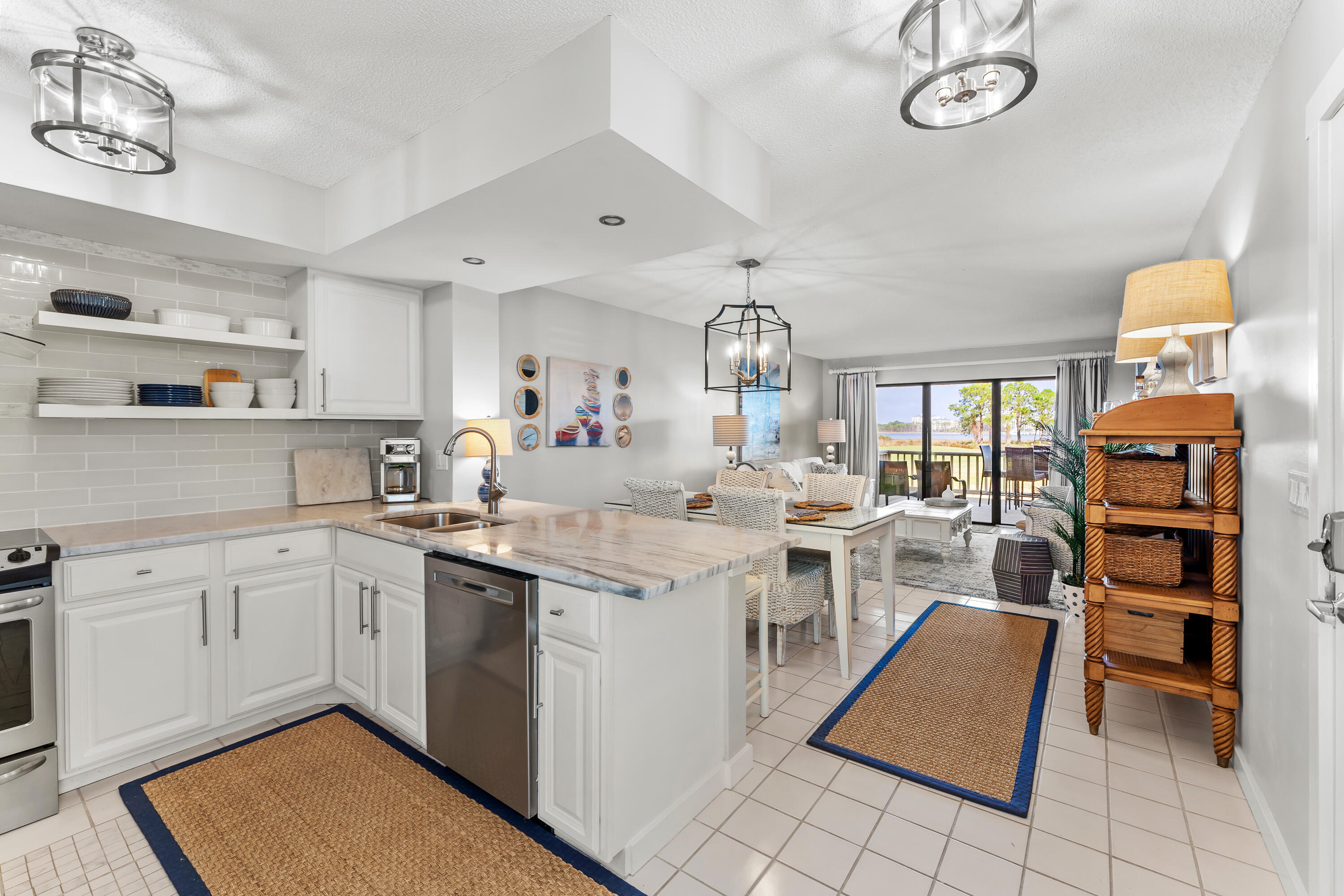 Open-plan kitchen and living area with a marble-look island and water visible through the sliding glass doors.