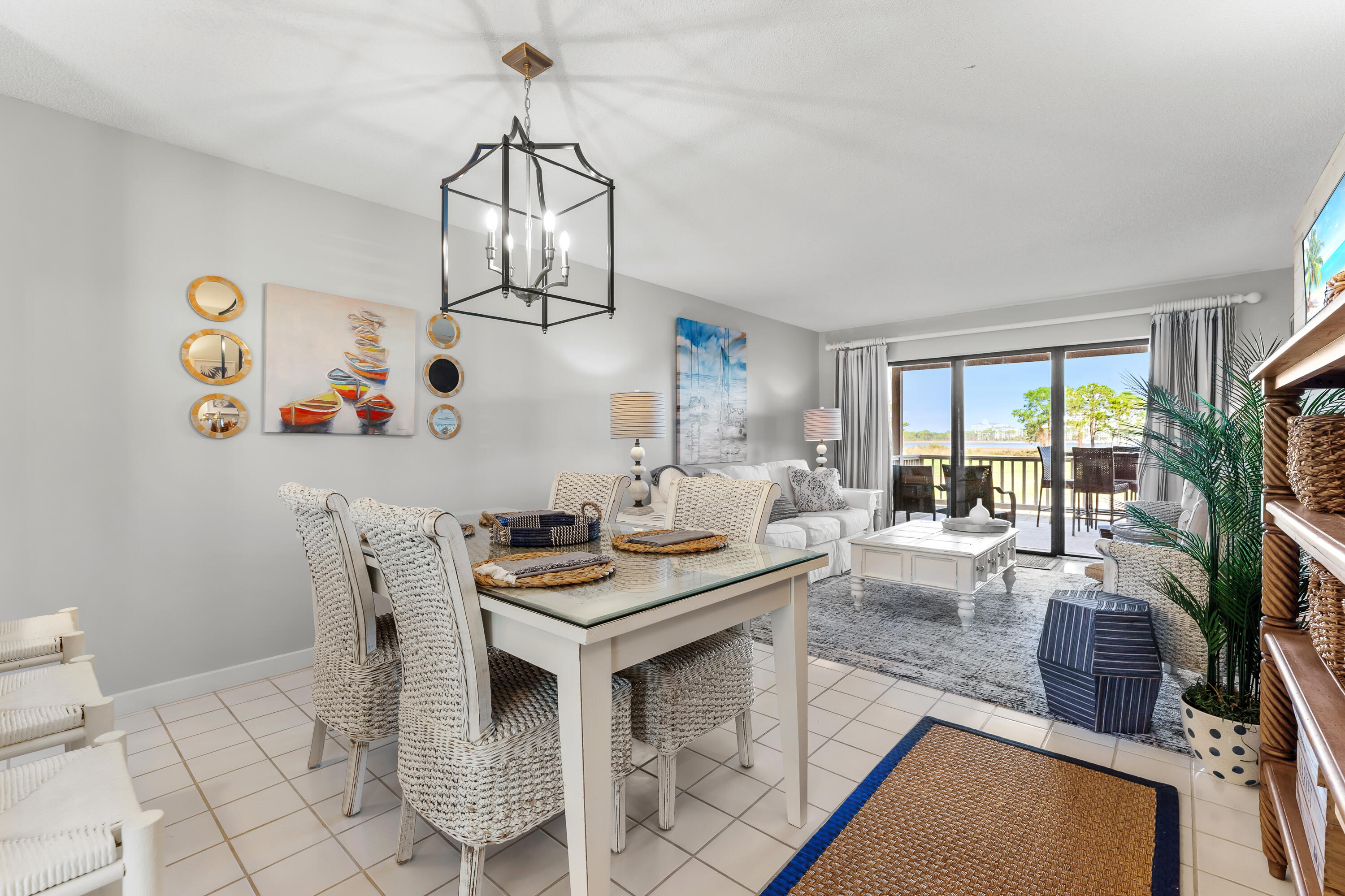 Dining and living room with woven chairs and a balcony overlooking water.