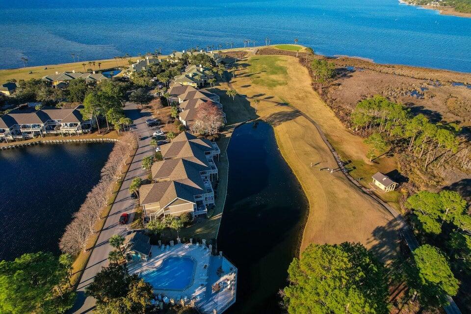 Aerial view of waterfront residences, a community pool, and grassy shoreline beside blue bay water.