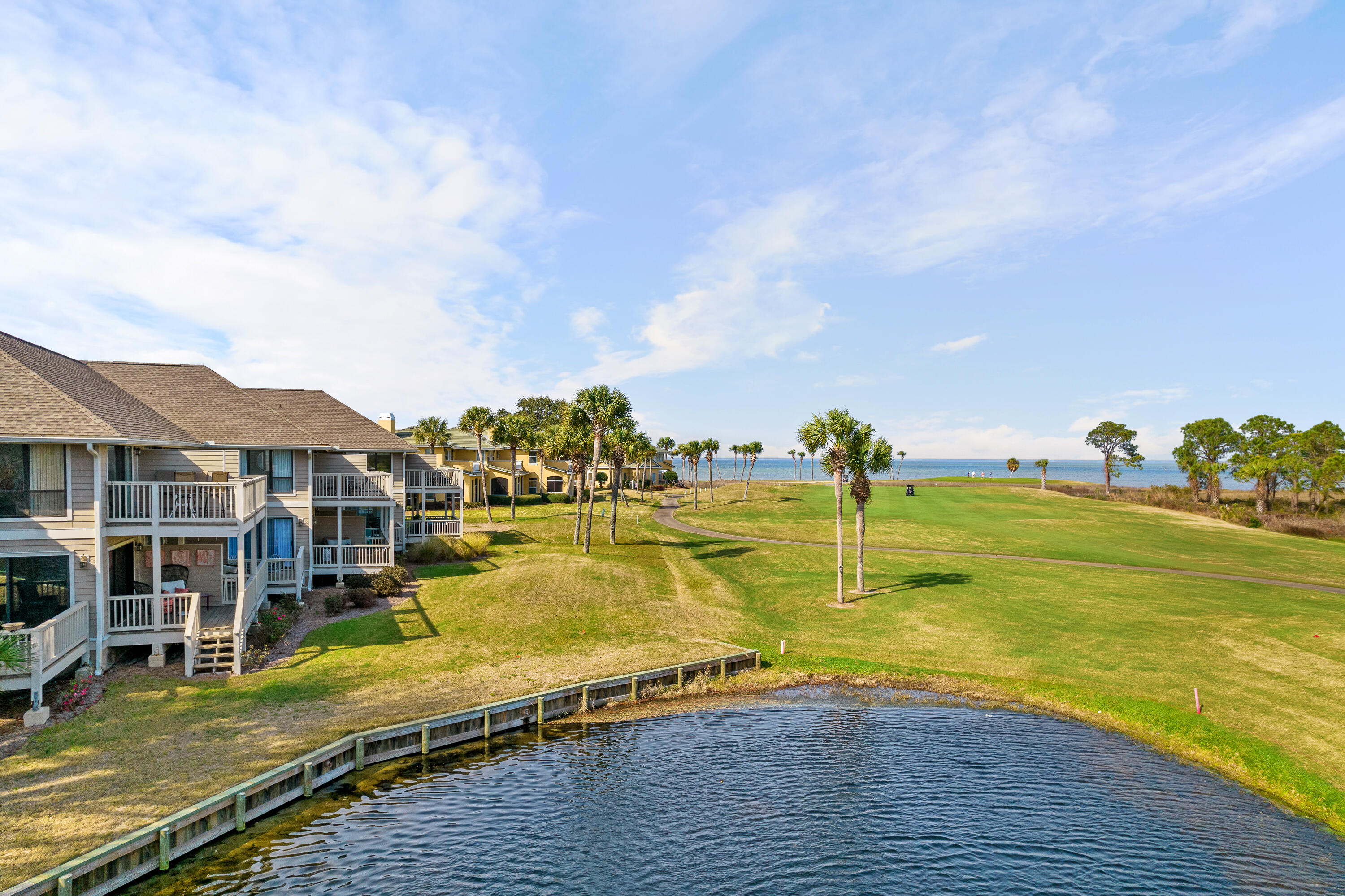 Coastal condominiums overlooking a palm-lined golf course, pond, and bay.
