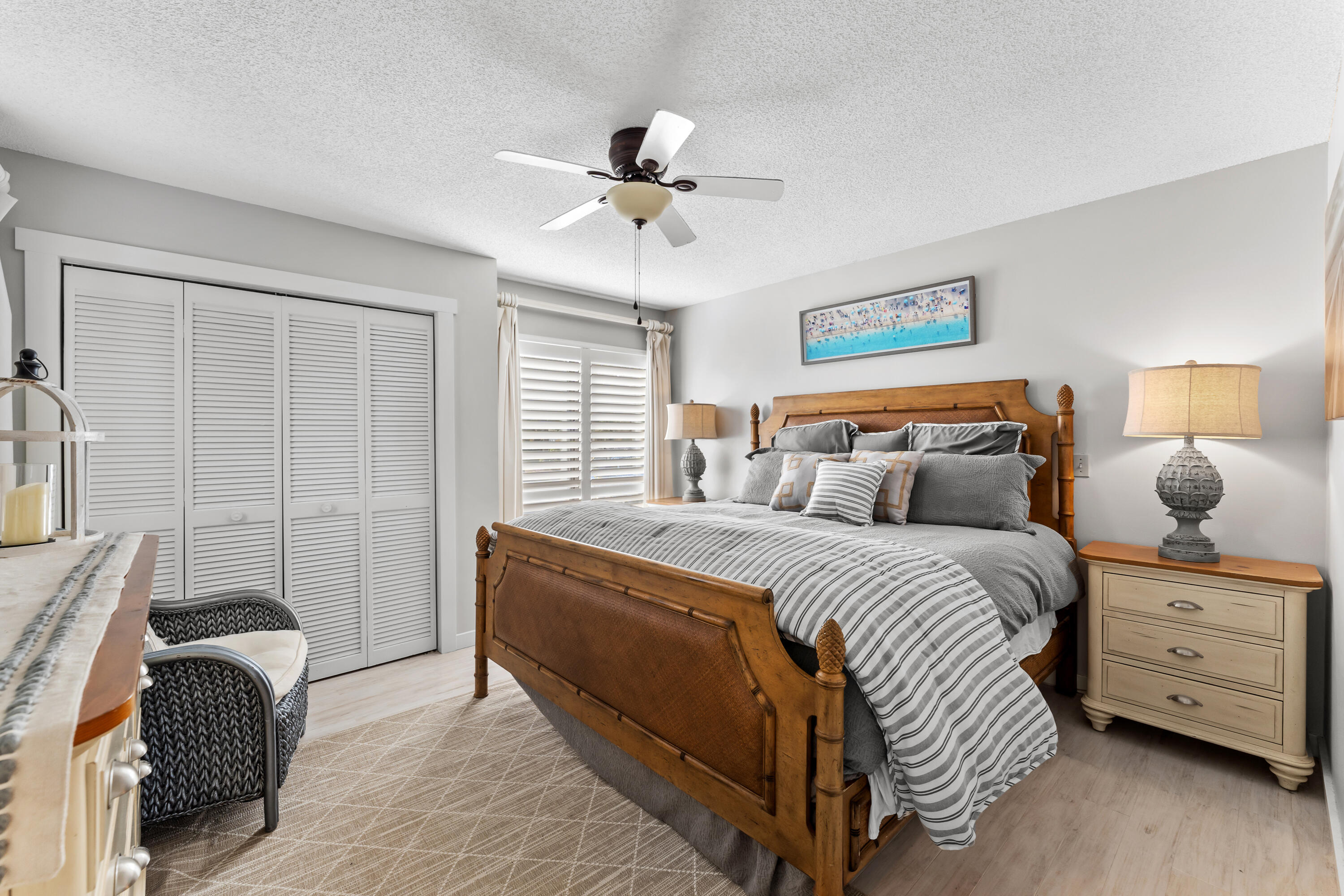 Bedroom with a wooden bed, gray striped bedding, and white plantation shutters.