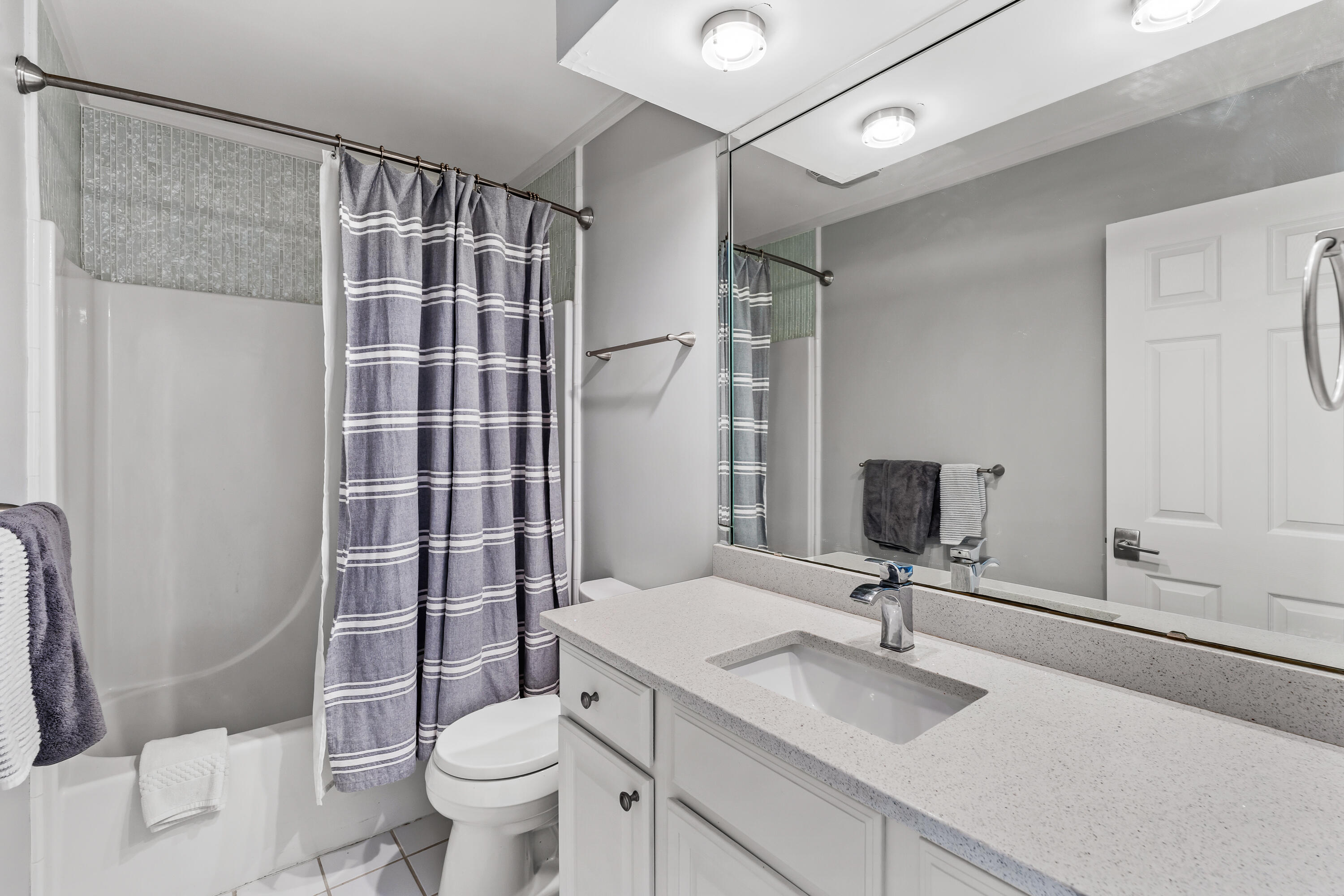 Bathroom with a gray striped shower curtain, bathtub, toilet, and white vanity with a large mirror.