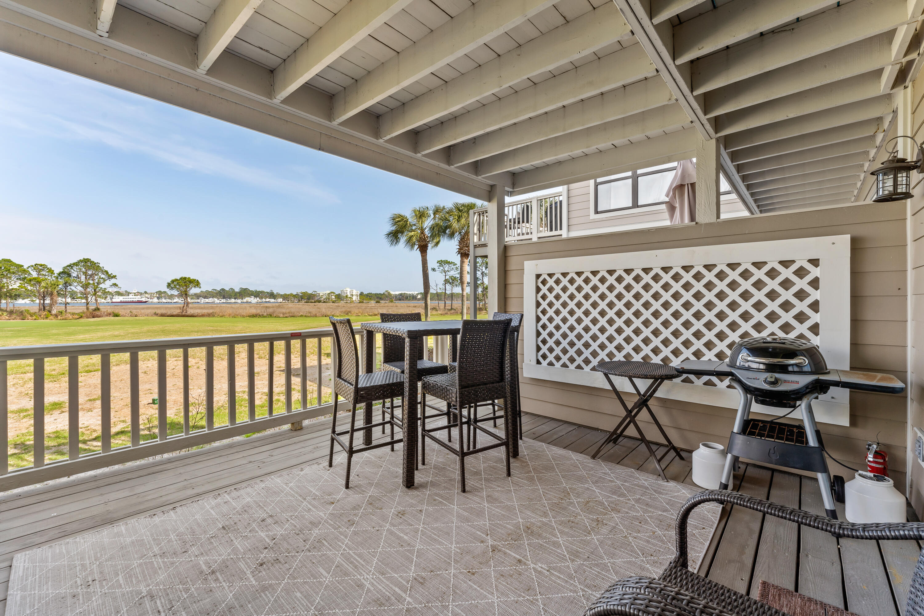 Covered deck with wicker dining set and grill overlooking marsh grasses and water.