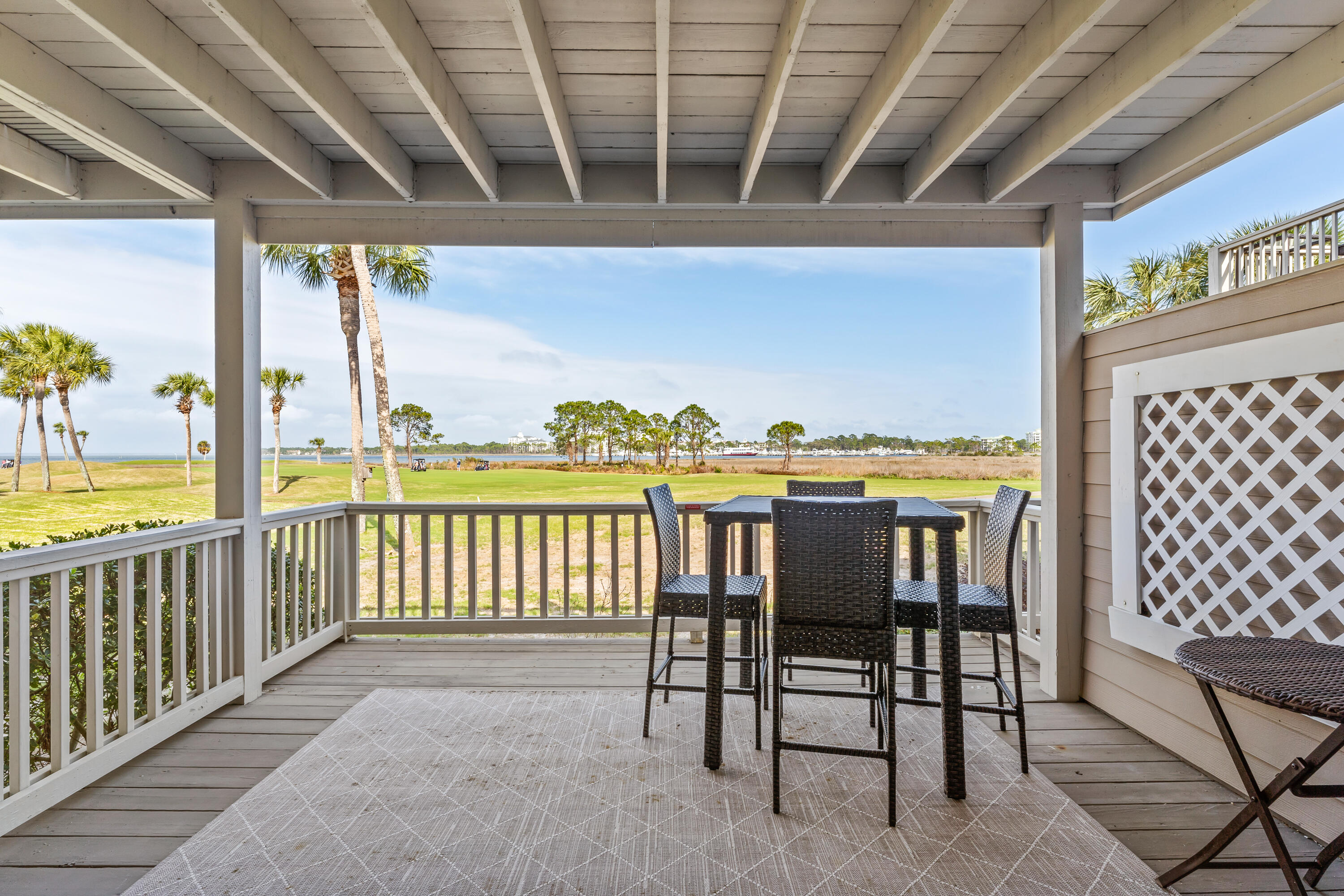 Covered patio with wicker dining set overlooking a palm-lined golf course and water.