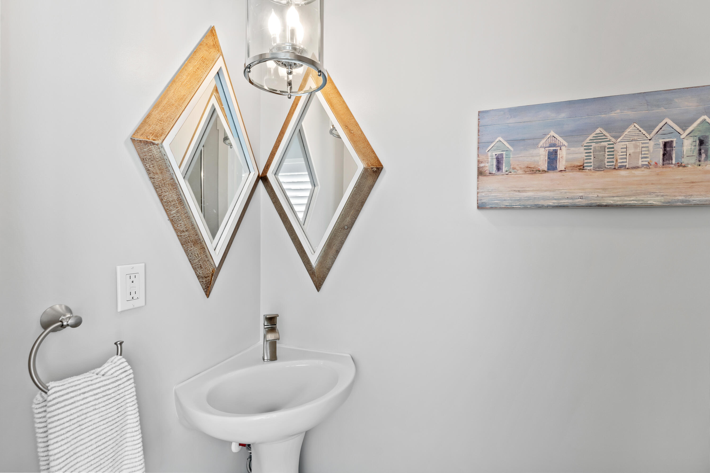 Bathroom sink beneath geometric wood-framed mirrors, with beach-hut artwork on the wall.