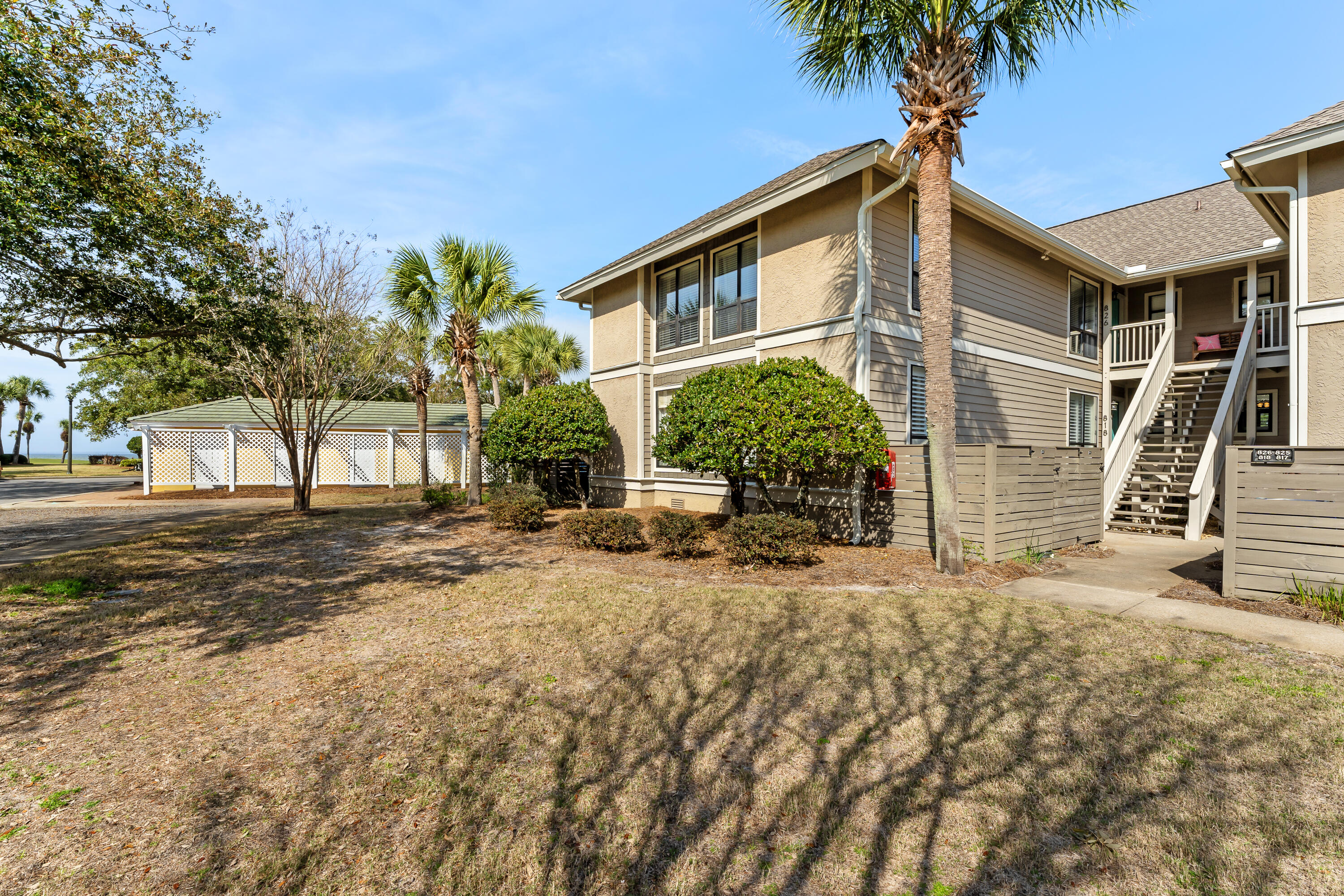 Two-story condominium with outdoor stairs, palm trees, and a glimpse of water.
