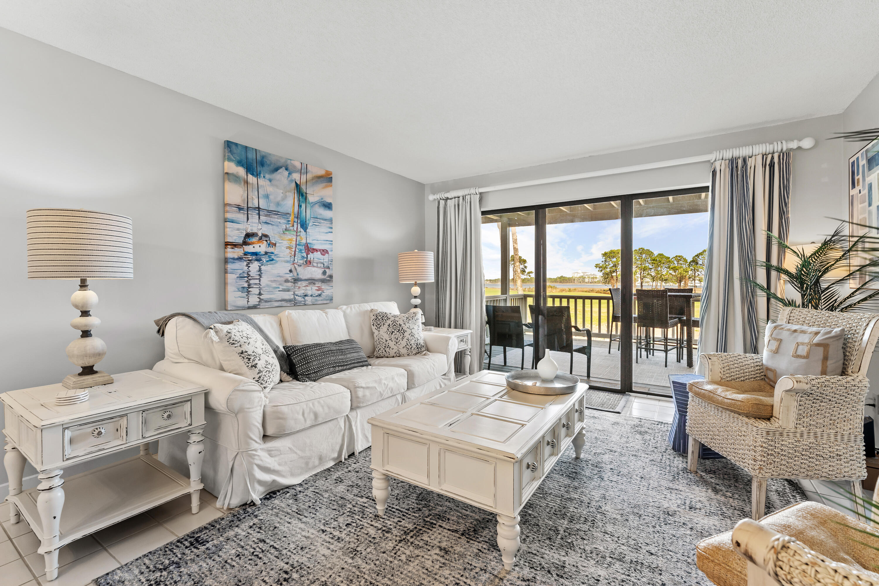 Living room with white furnishings and sliding doors opening to a balcony overlooking the water.