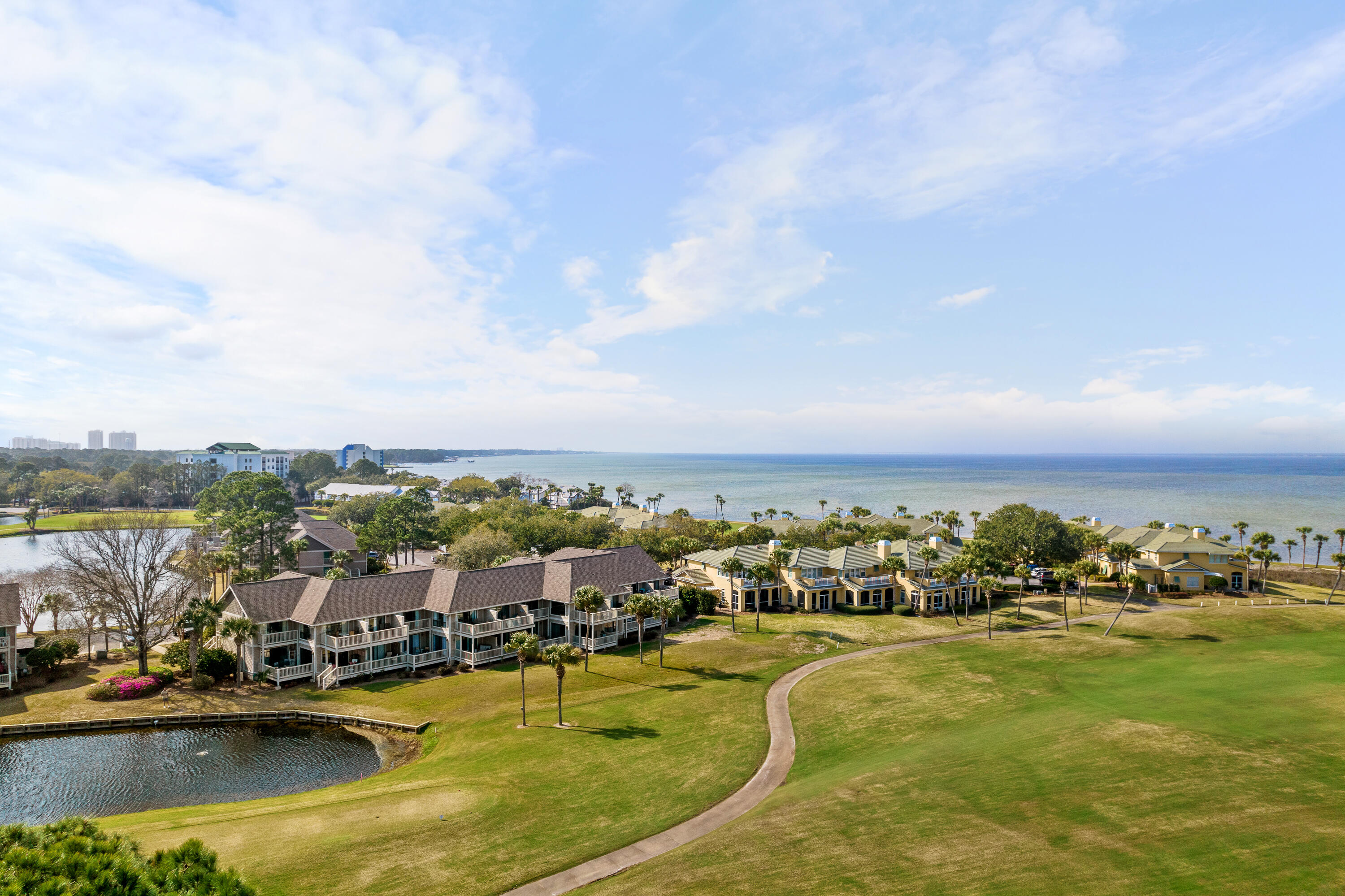 Coastal condominiums beside a broad lawn, pond, and Gulf shoreline.