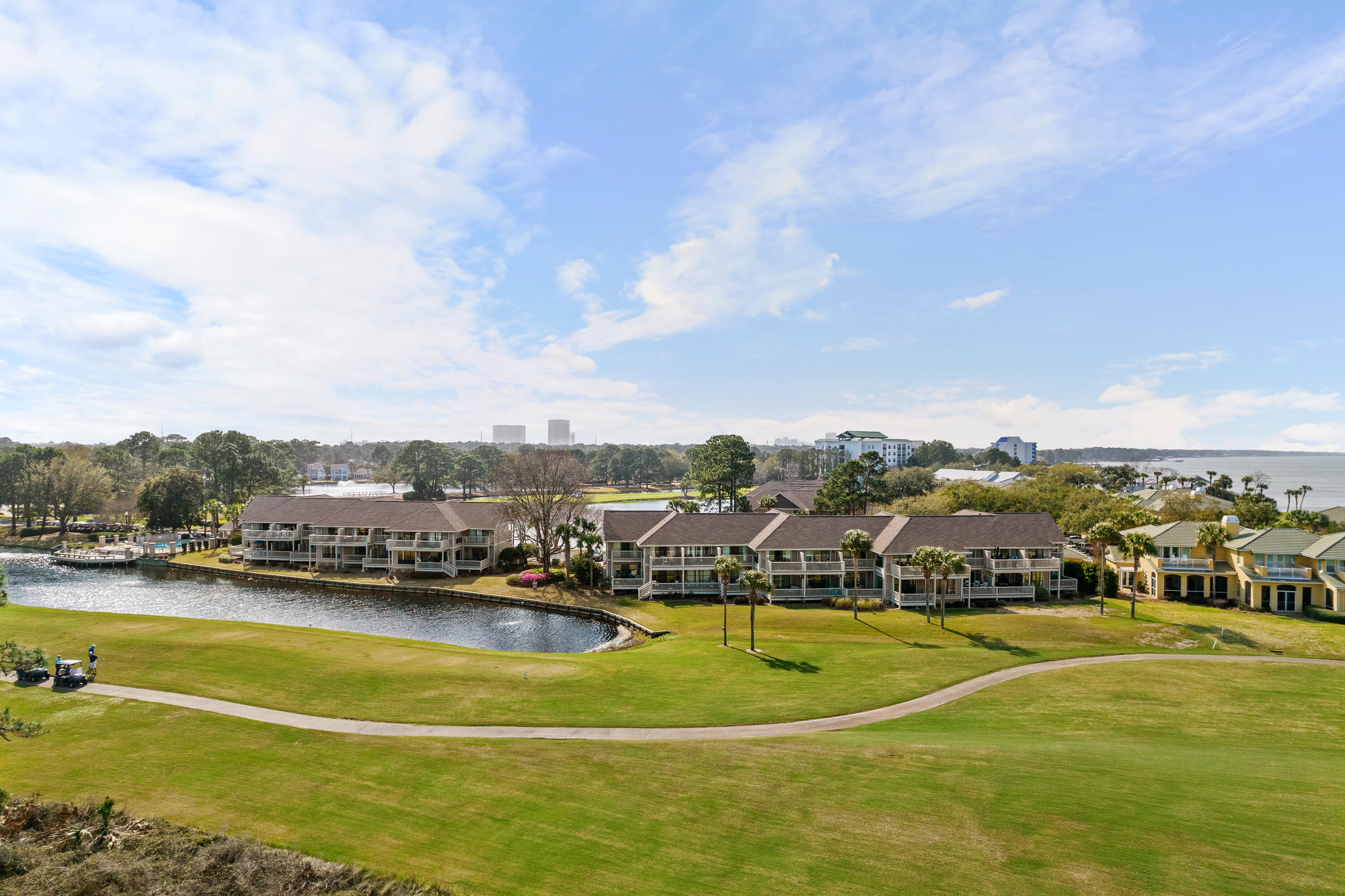 Waterfront condominiums beside a green golf course, with a winding waterway and bay in the distance.