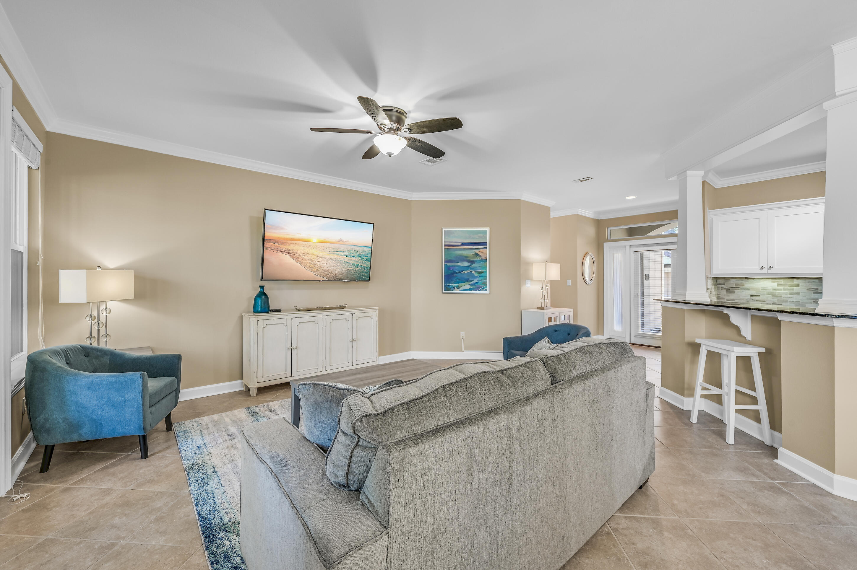 Living room with gray sectional, blue accent chairs, ceiling fan, and adjoining kitchen.