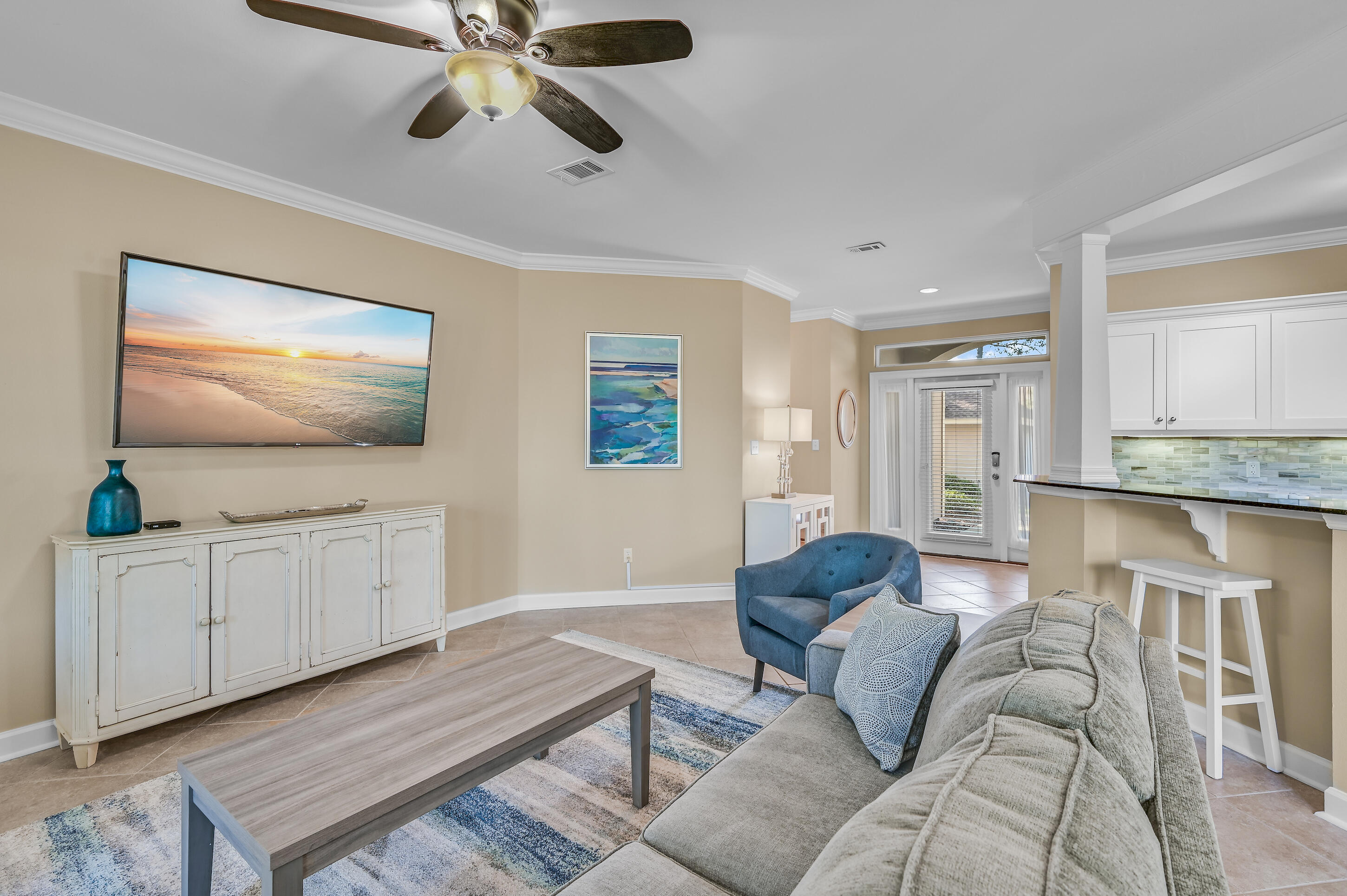 Furnished living room with a blue accent chair, ceiling fan, and open kitchen breakfast bar.