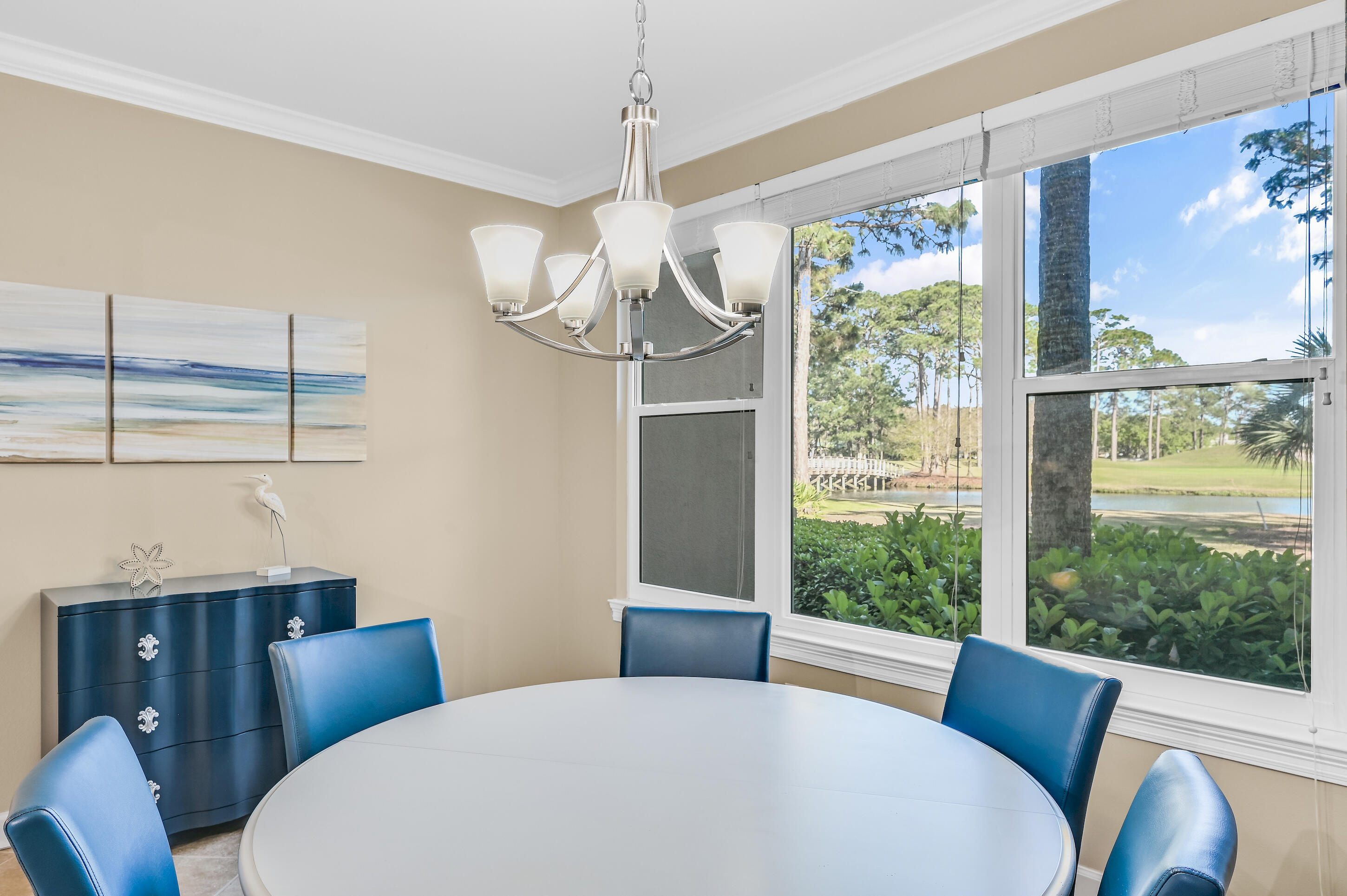 Dining room with a round white table and blue chairs overlooking a pond through large windows.
