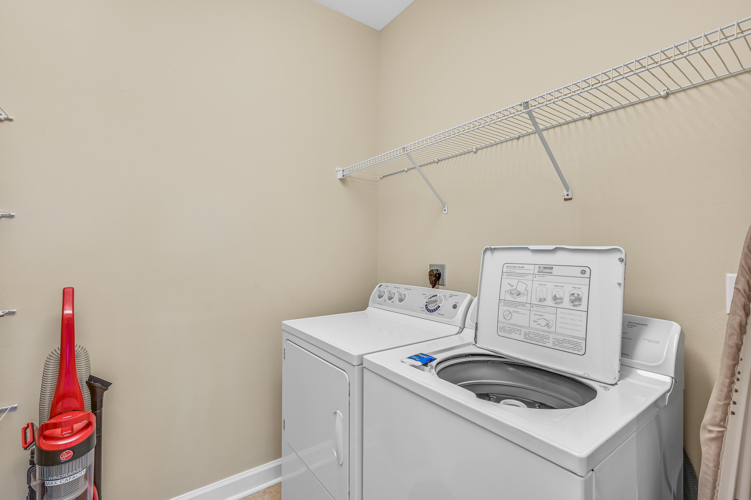 Laundry room with a top-loading washer and dryer beneath wall-mounted wire shelving.