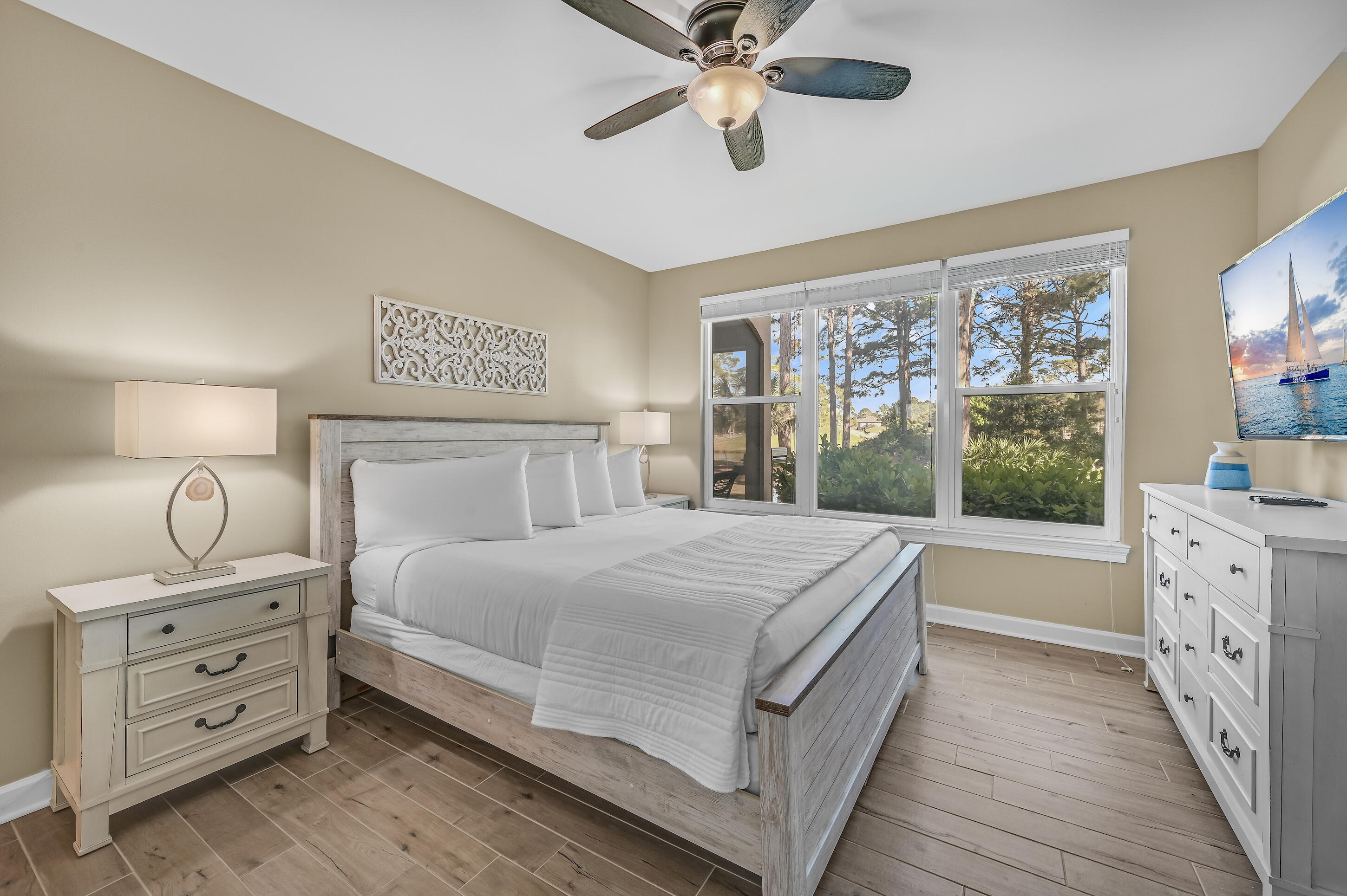 Furnished bedroom with a gray wood bed and wide windows overlooking trees.