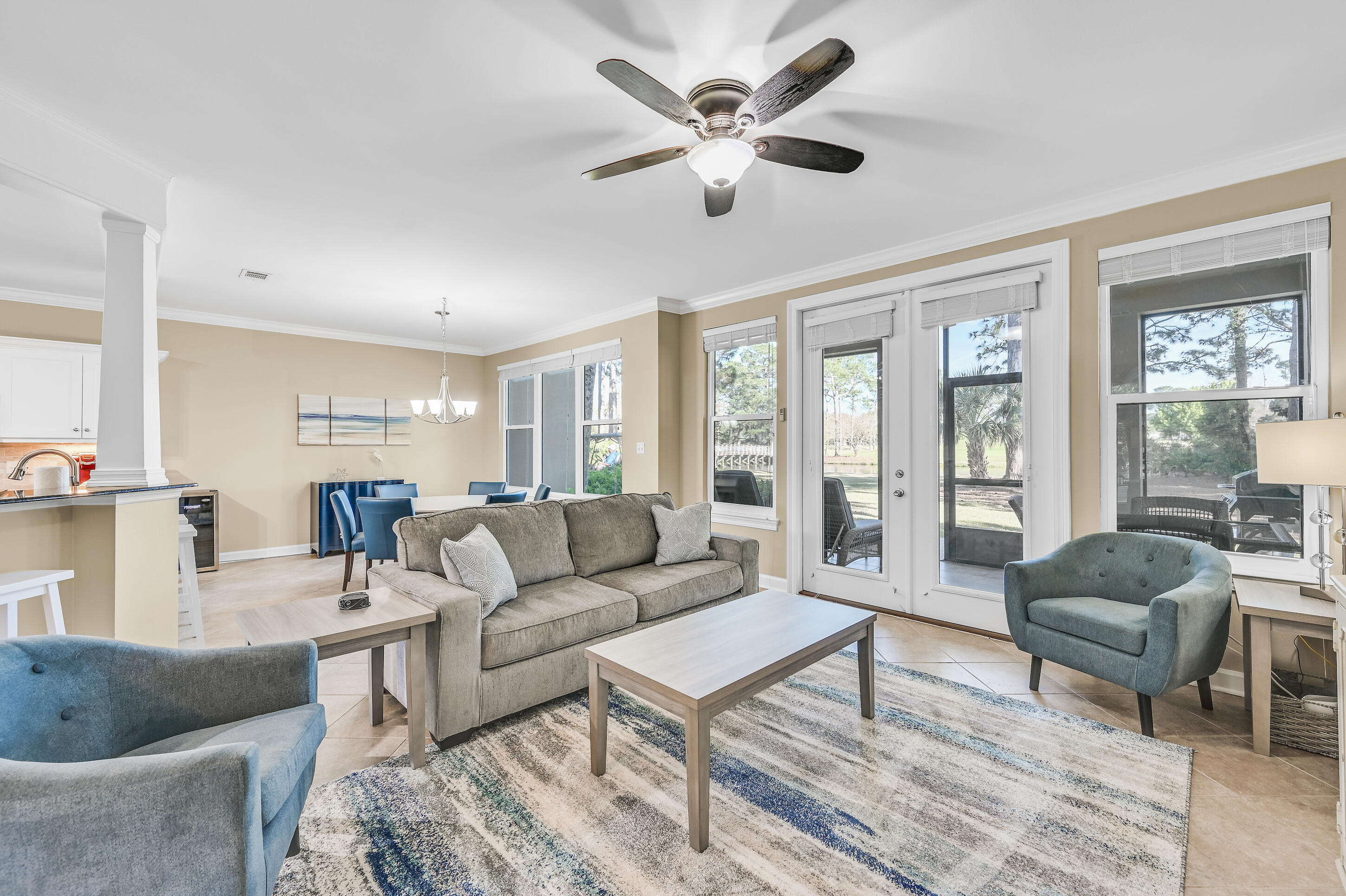 Furnished living room with a gray sofa, blue armchairs, and glass doors overlooking a green yard.
