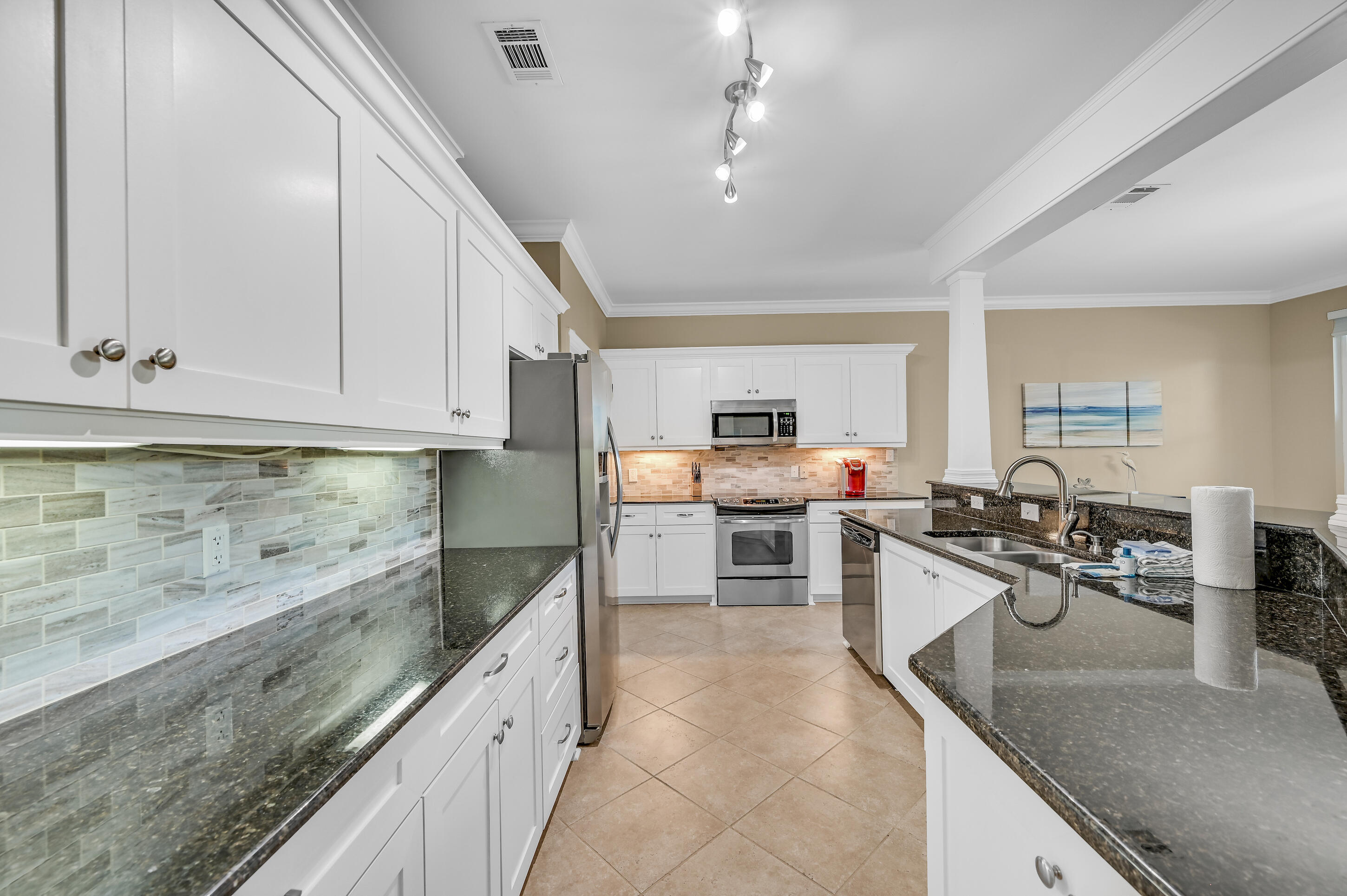 Kitchen with white cabinetry, stainless steel appliances, dark granite counters, and a double-sink peninsula.