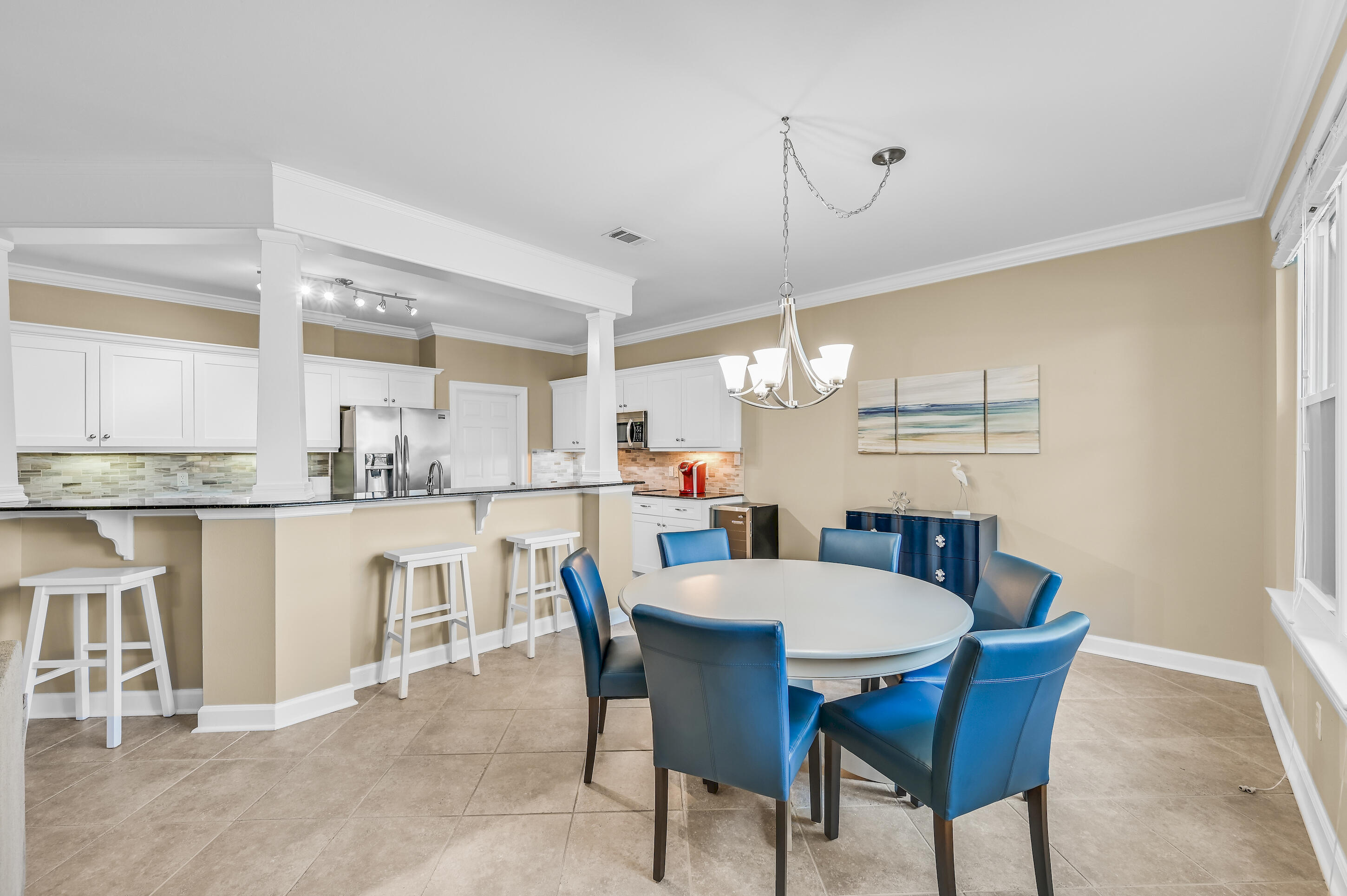 Kitchen and dining area with a white breakfast bar and round table surrounded by blue chairs.