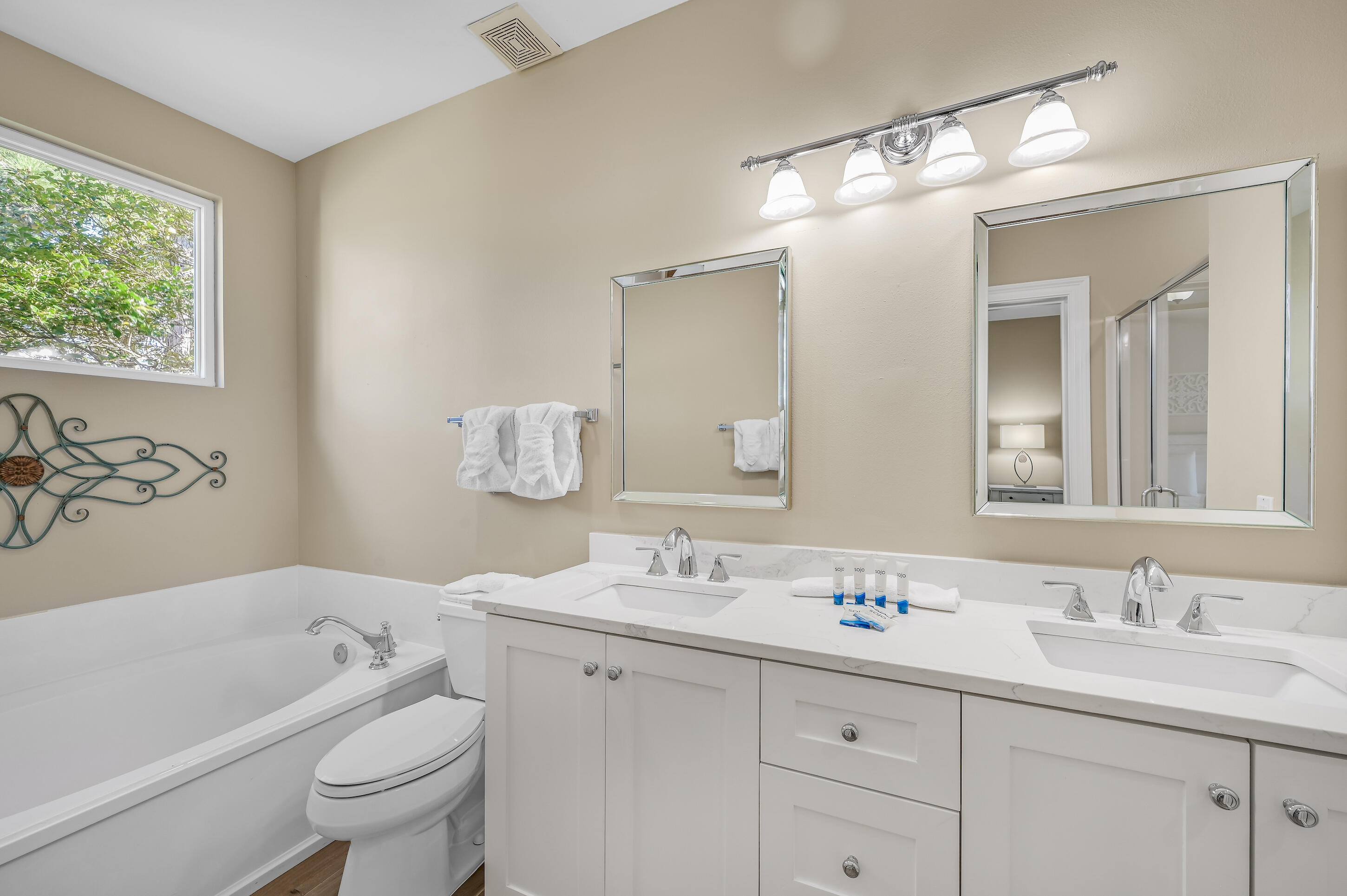 Bathroom with a white tub and toilet beside a double-sink vanity and large mirrors.
