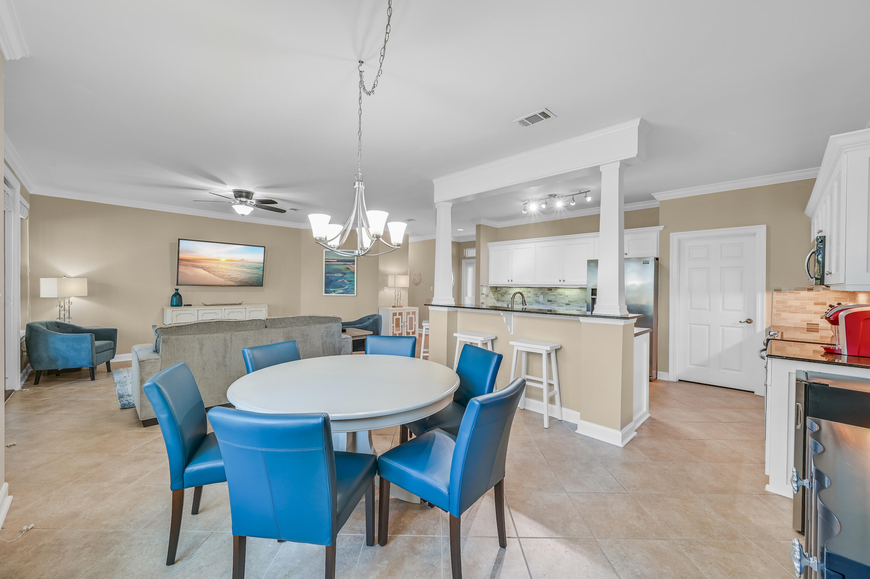 Open-plan dining area with a round white table and blue chairs beside the kitchen and living room.