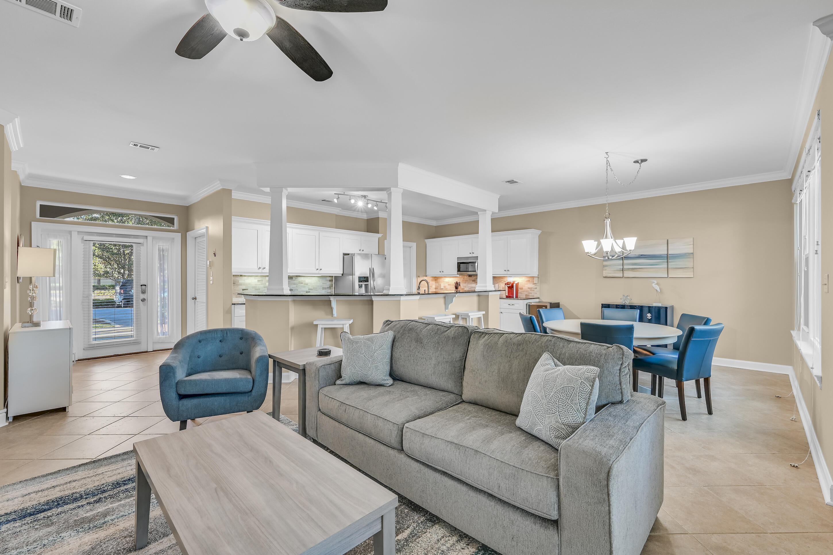 Open-plan living room with gray sectional, blue accent chair, and adjoining white kitchen.