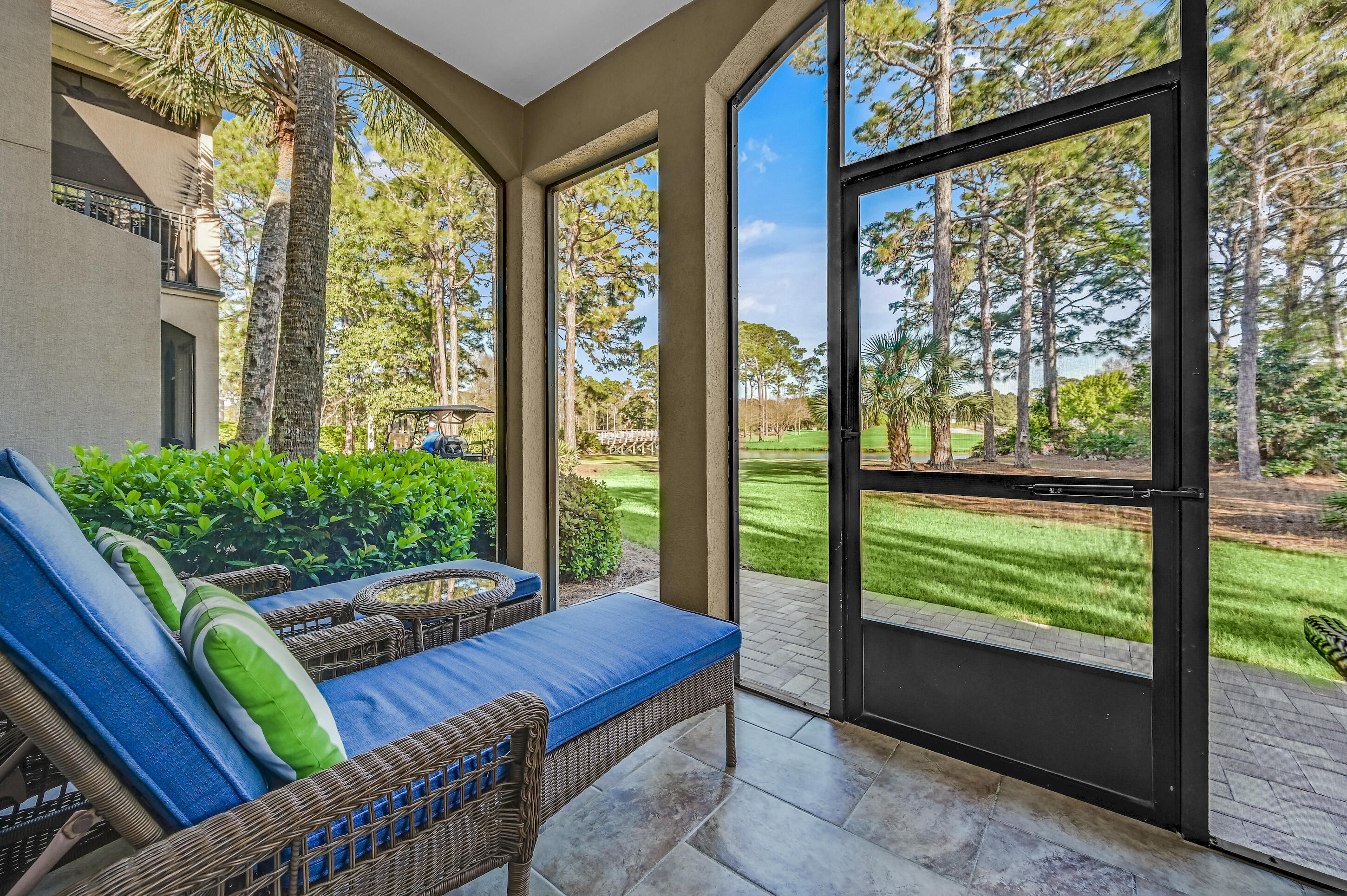 Screened porch with blue wicker seating overlooking a green lawn, palm trees, and pines.