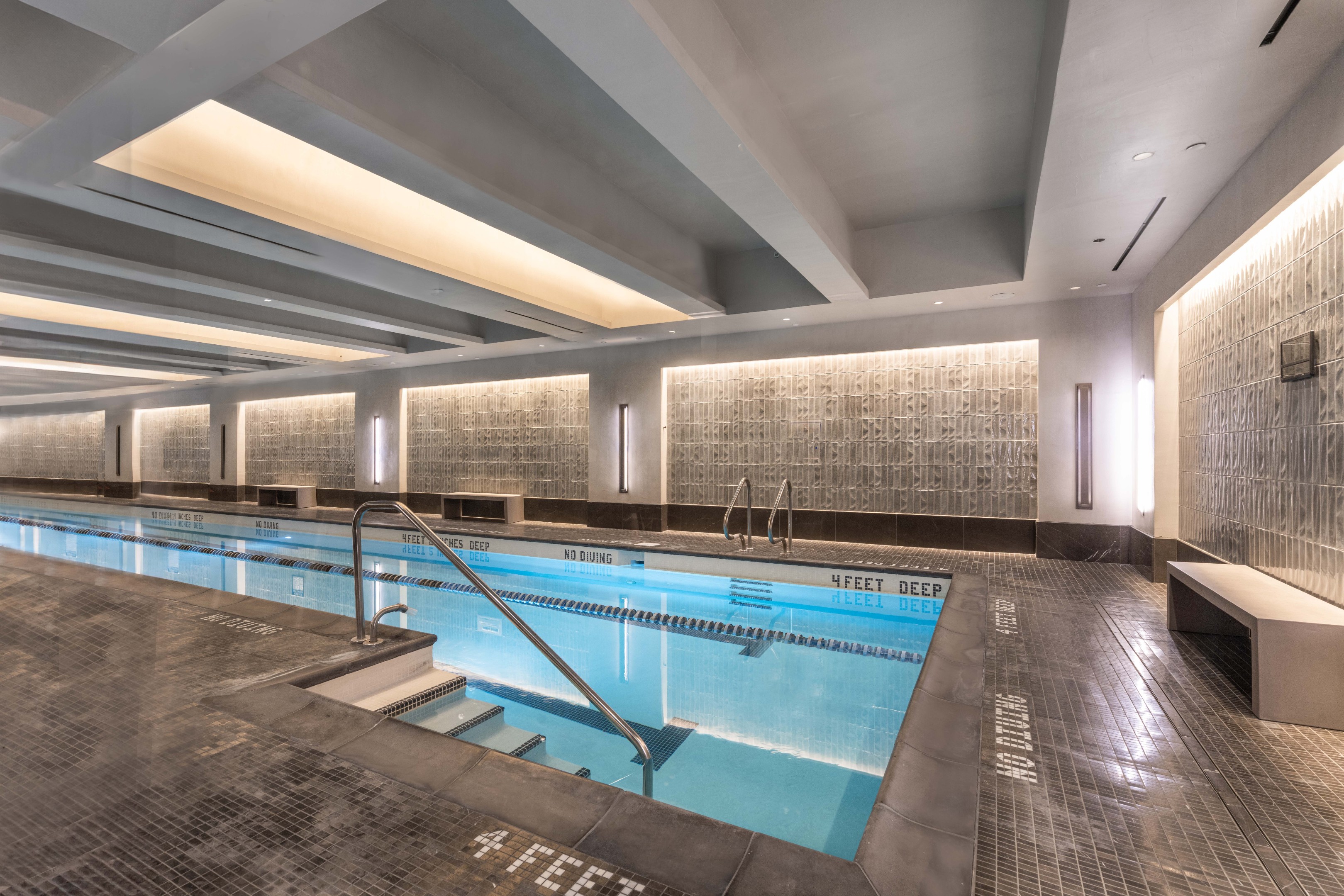 Indoor residential pool with blue water, tiled walls, and steps with metal handrails.