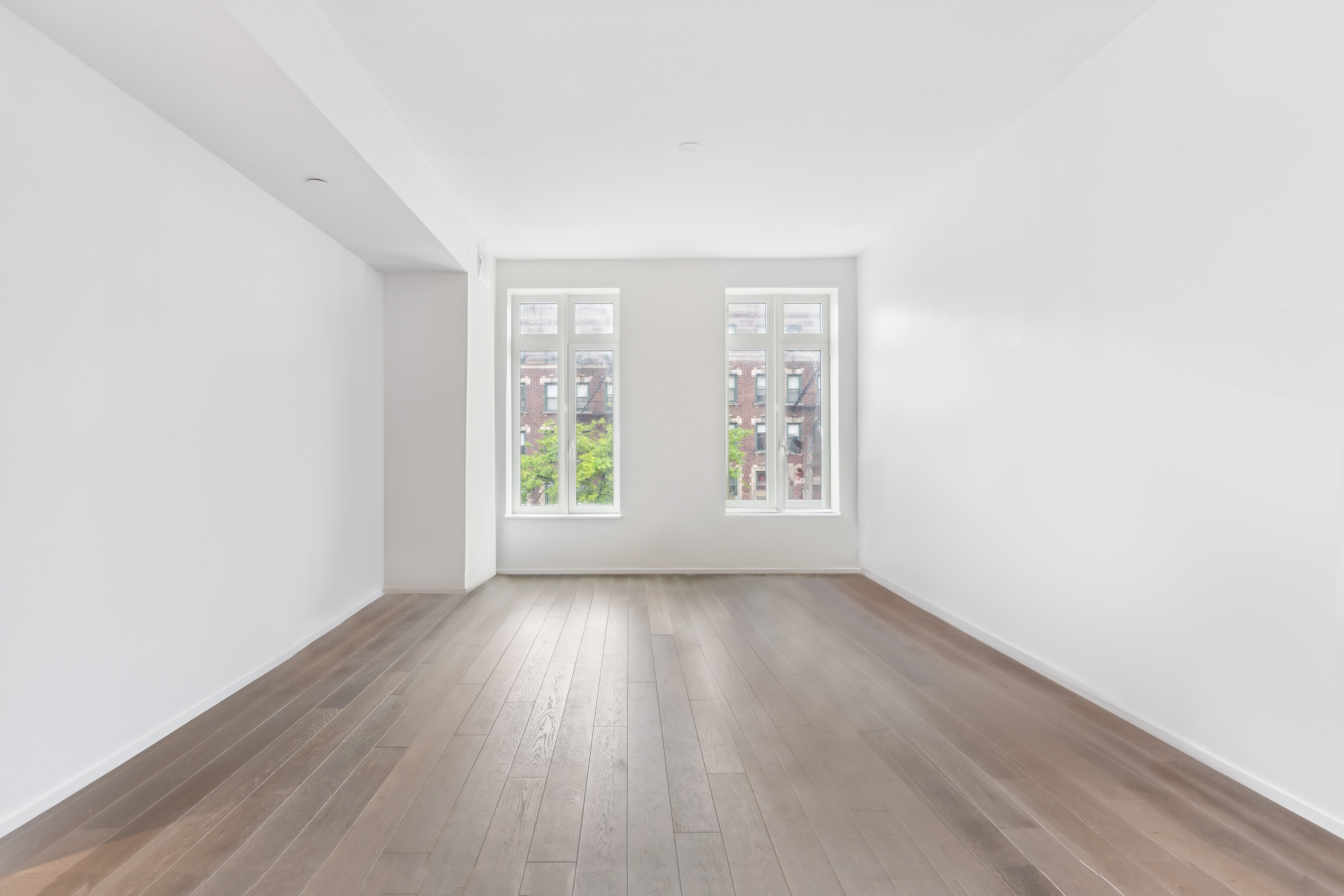 Vacant living room with wide-plank wood floors and two tall windows.