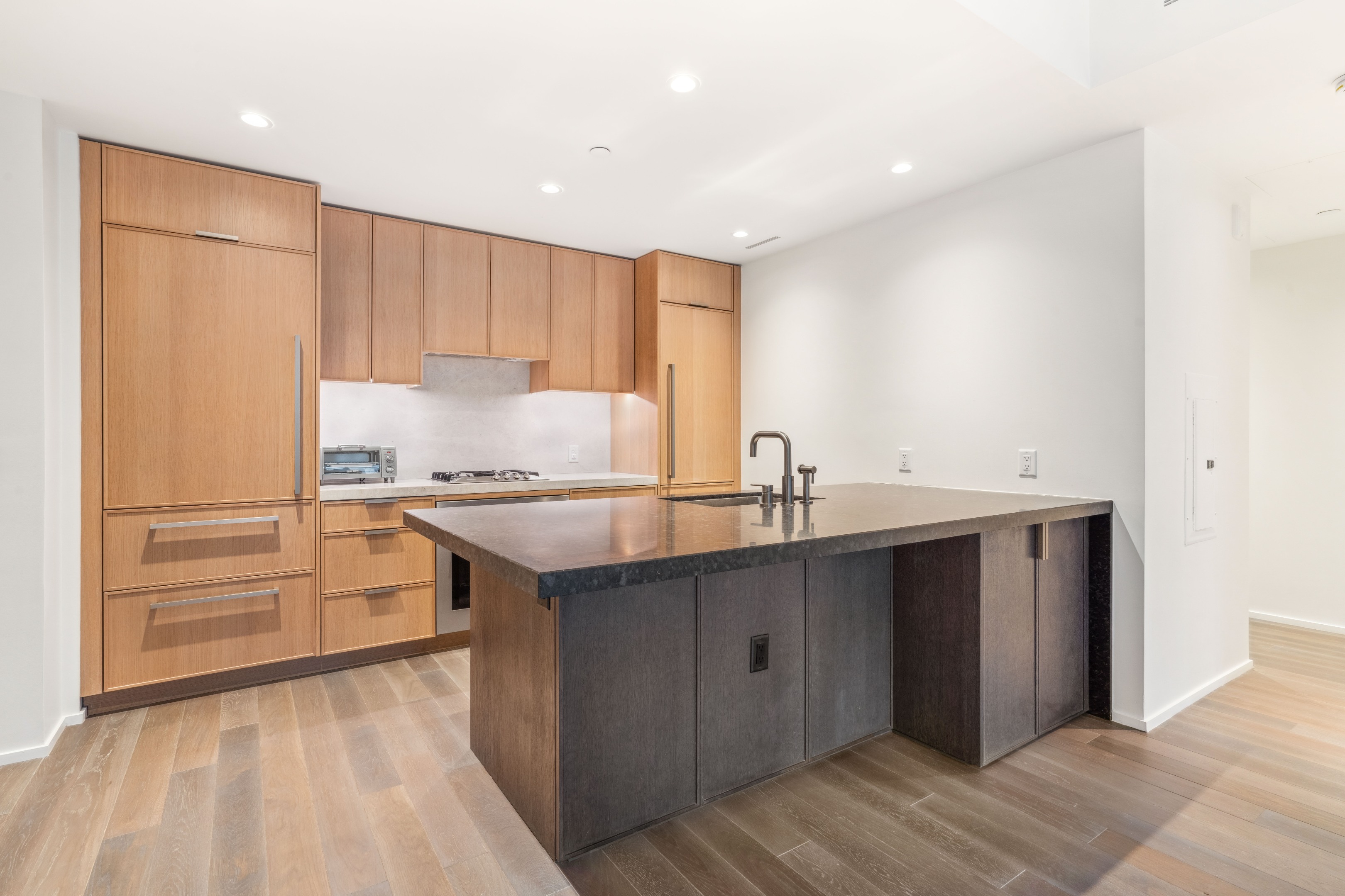 Modern kitchen with light wood cabinetry and a large dark island with a stone countertop.