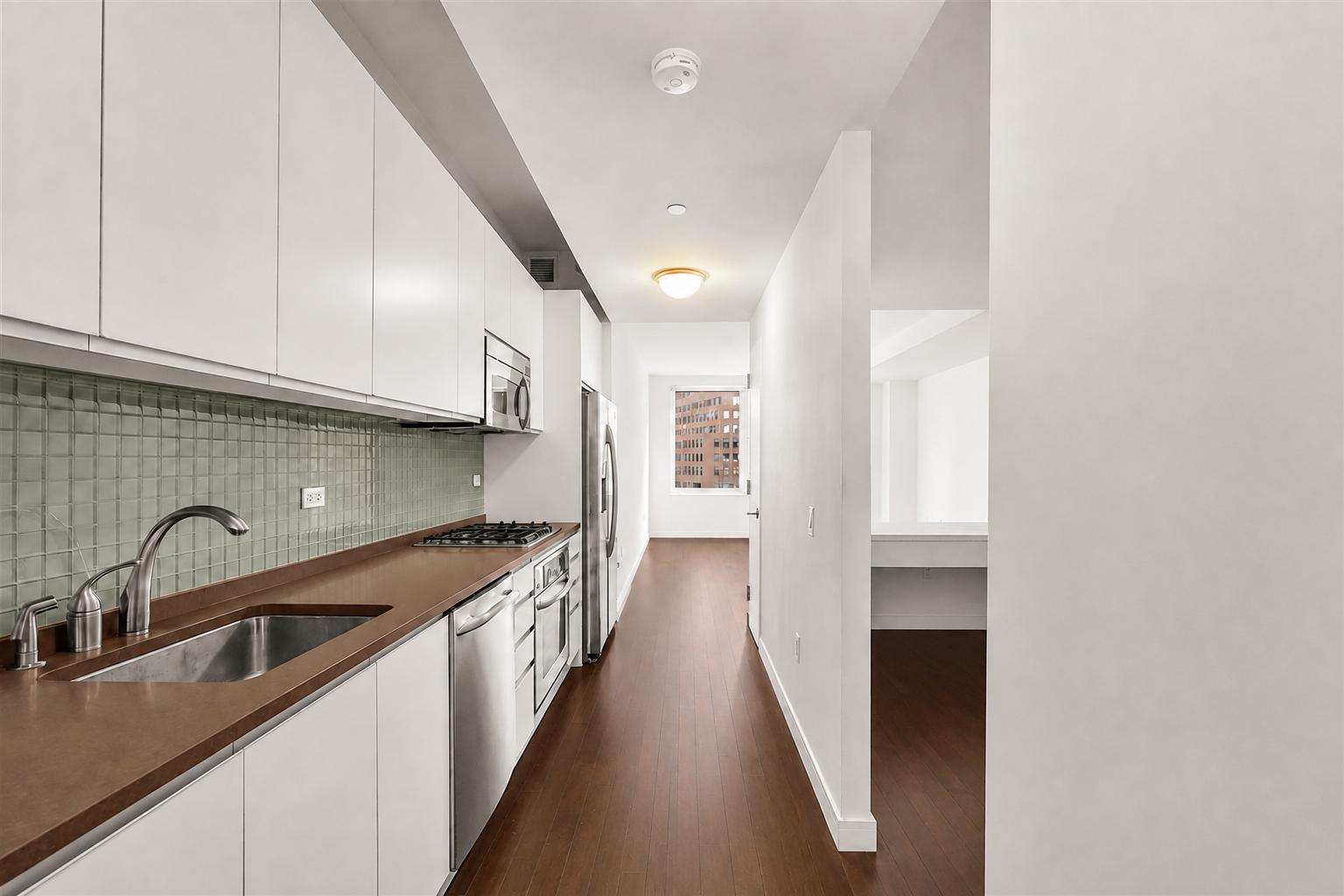 Galley kitchen with white cabinets, stainless steel appliances, brown counters, and dark wood floors.