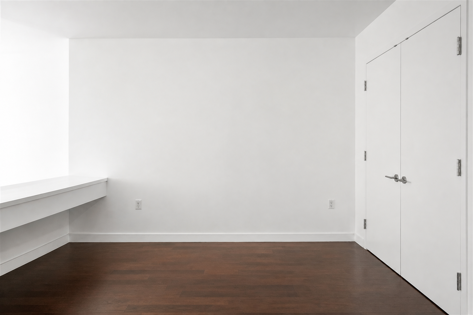 Empty room with dark wood floors, a built-in desk, and double doors.
