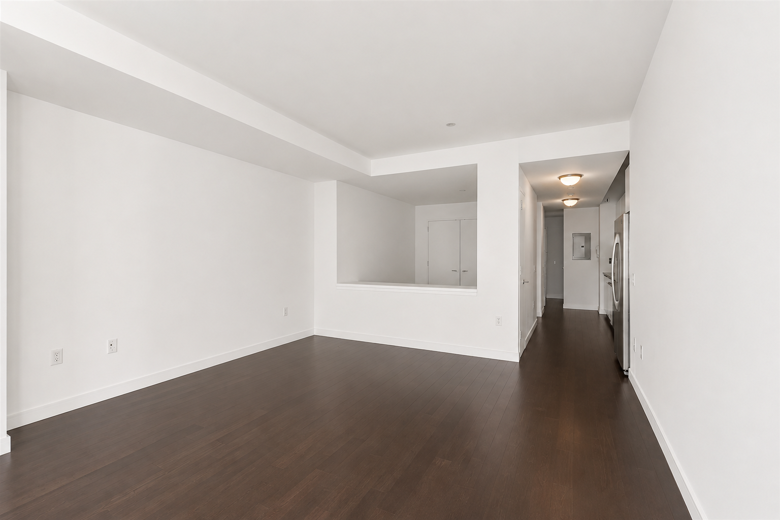 Vacant living area with dark hardwood floors and a kitchen pass-through.