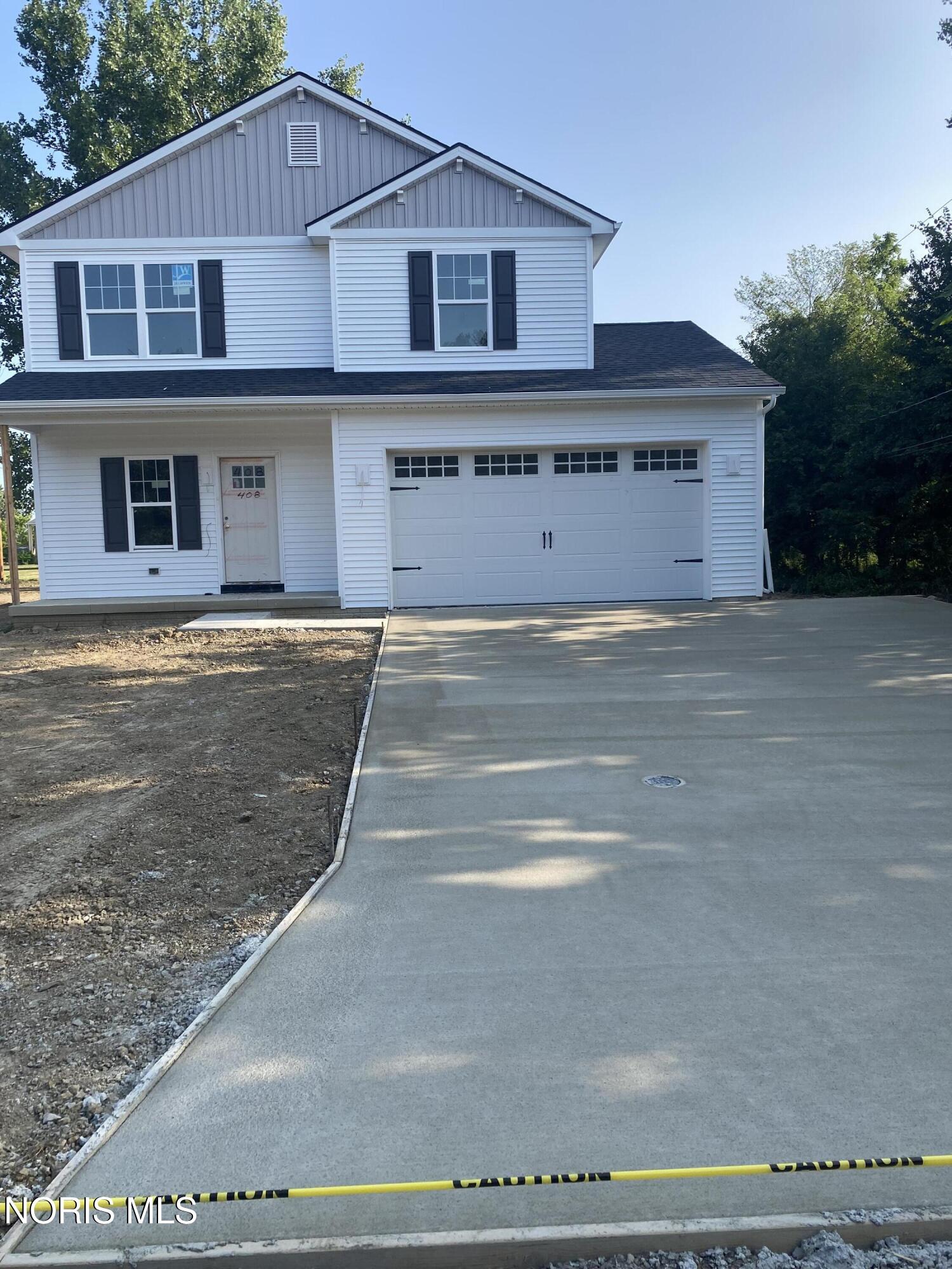Two-story white house with black shutters and a broad concrete driveway bordered by unfinished ground.