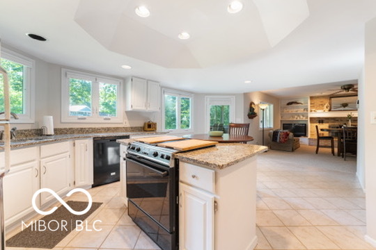 Open kitchen with a granite island, stainless-steel range, and windows overlooking greenery.