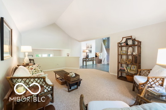 Living room with vaulted ceiling, wicker seating, and a tall wooden bookcase.