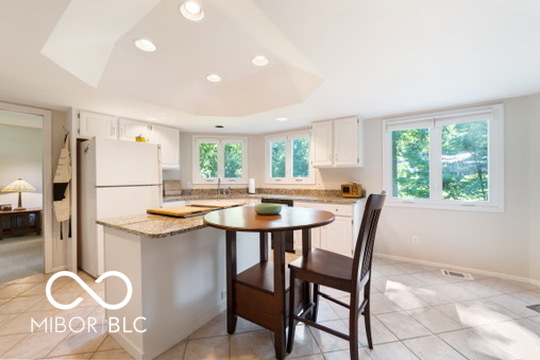 Kitchen with white cabinets, granite island, and a small dining table beside large windows.