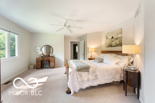 Bedroom with pale patterned bedding, dark wood nightstand, and vanity beneath a round mirror.