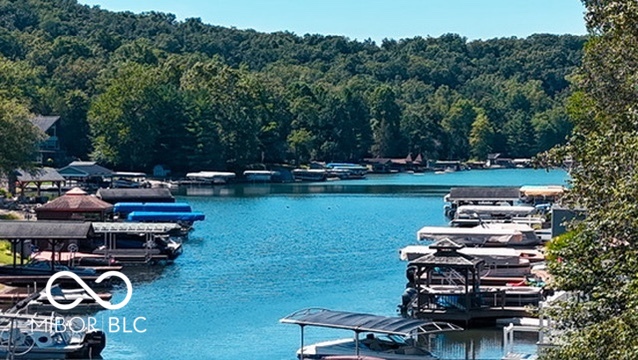 Lake marina with covered boat docks and moored boats along a wooded shoreline.
