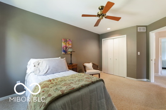 Bedroom with a patterned quilt, ceiling fan, and white closet doors.