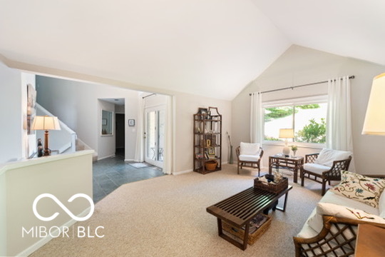 Living room with a vaulted ceiling, neutral carpet, and seating arranged around wooden coffee tables.
