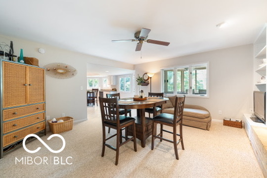 Dining area with a wooden table, wicker-front cabinet, and windows overlooking greenery.