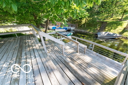 Wooden waterfront dock with metal railings, leafy shade, and boats moored nearby.