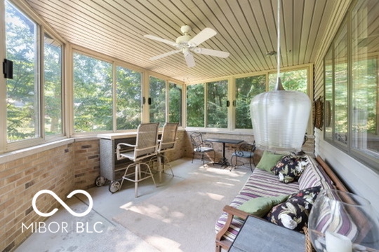 Enclosed sunroom with wraparound windows, a brick half wall, and cushioned seating.